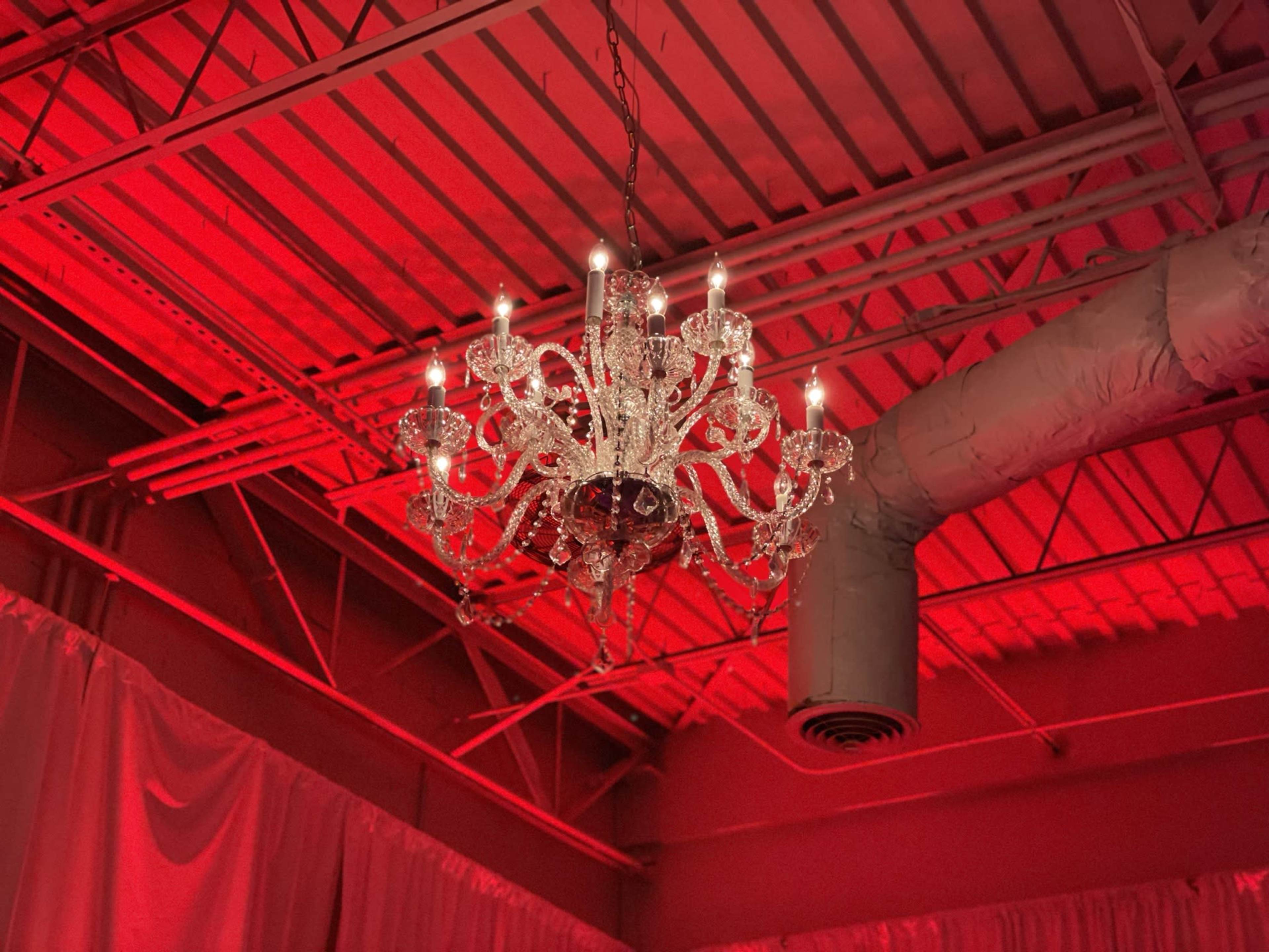 A chandelier with multiple lights hangs from a red-lit ceiling in an industrial space.