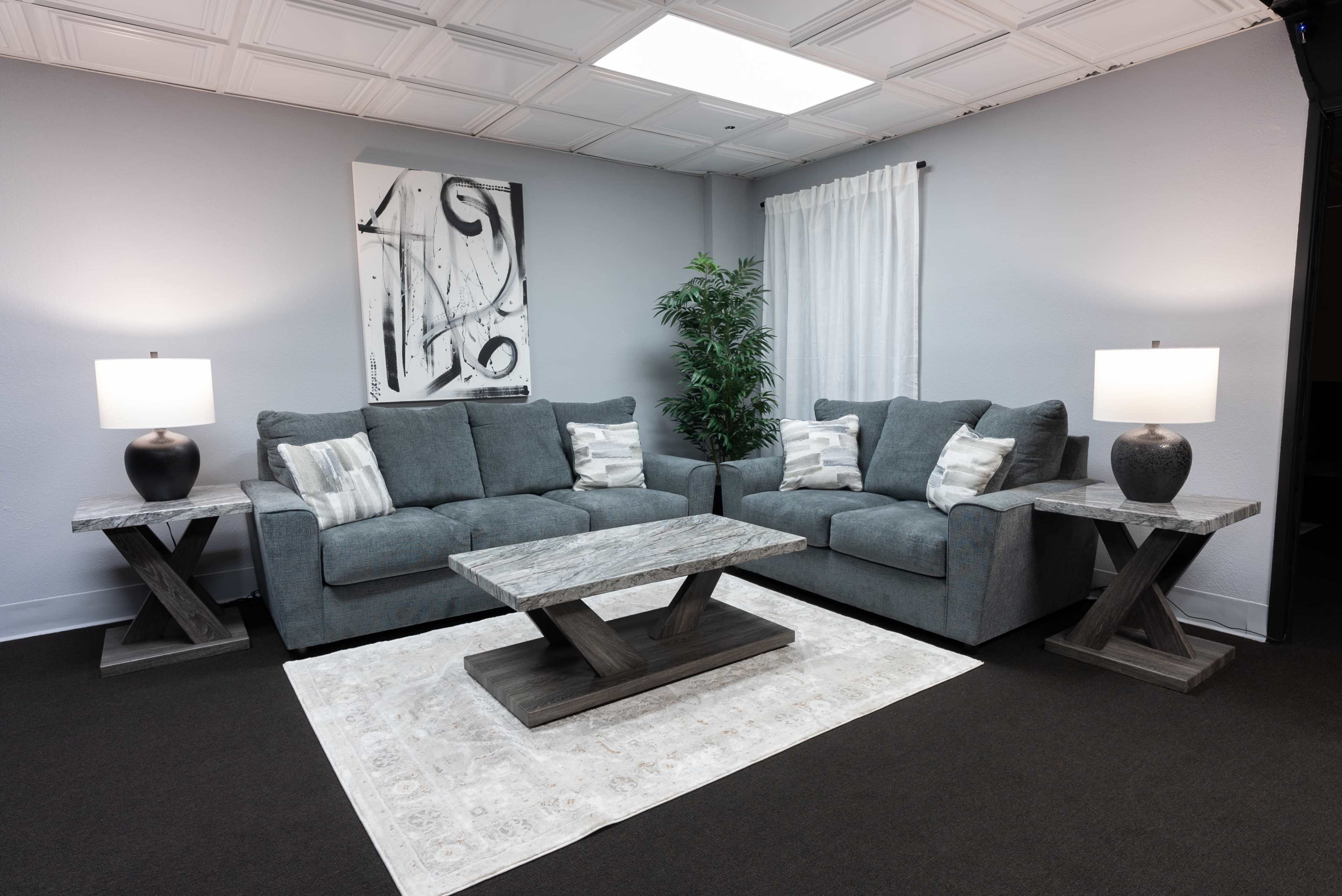 A modern living room with a gray sectional sofa, two matching side tables with lamps, a decorative coffee table, and a light-colored area rug.