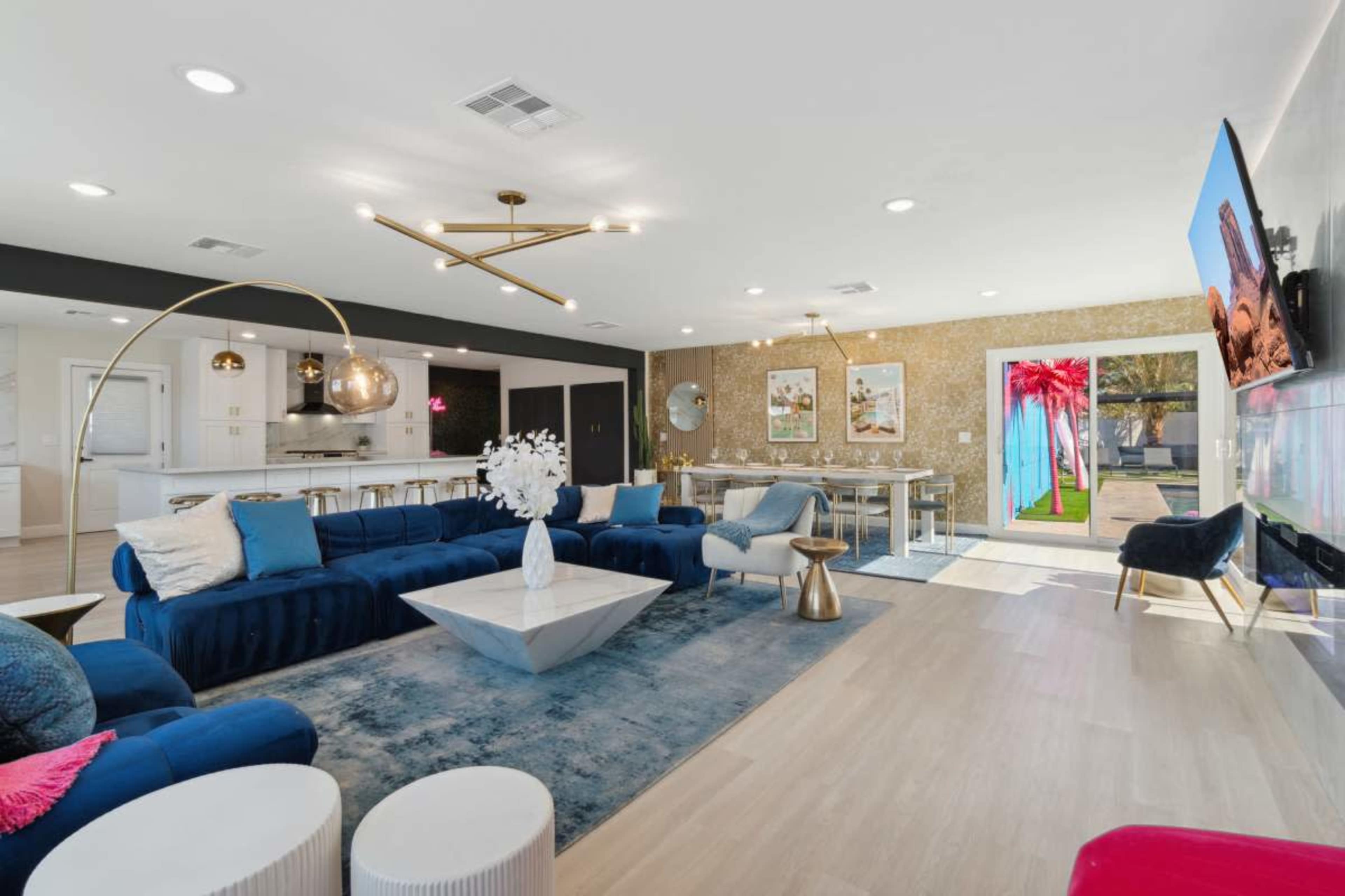 The living area features a modern design with a blue sectional sofa, a geometric coffee table, and a dining area visible in the background.