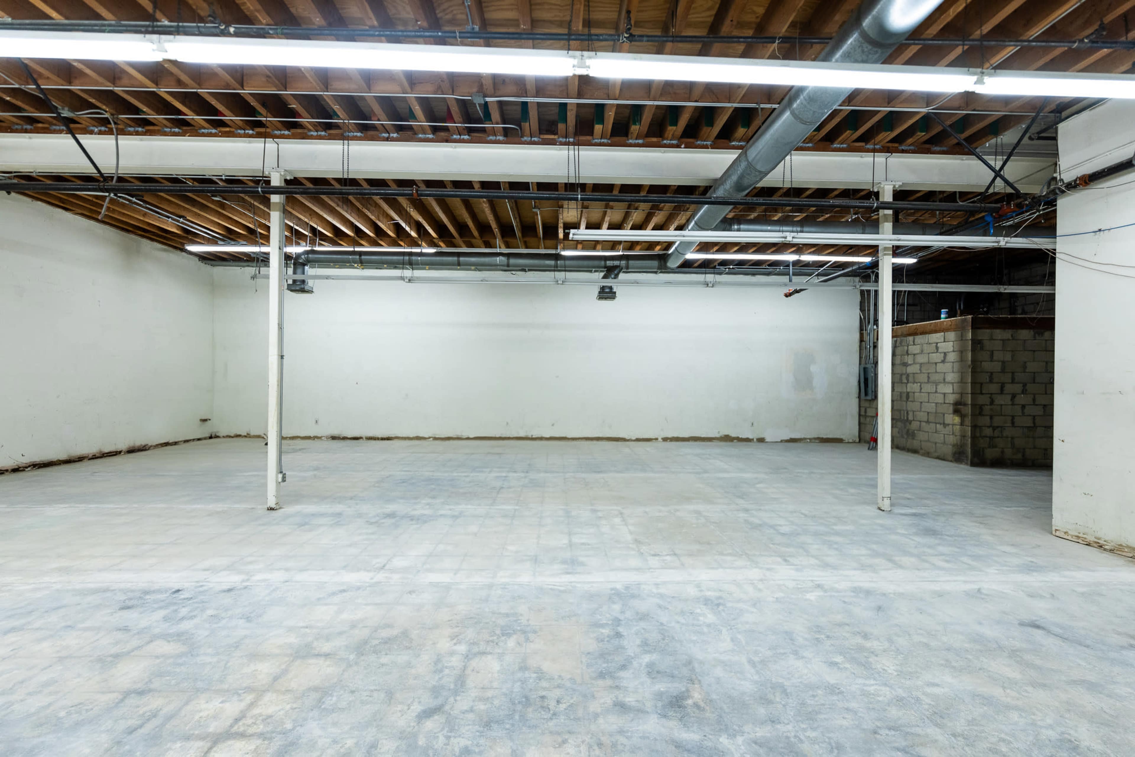 The image shows an empty warehouse space with exposed wooden beams and concrete flooring.