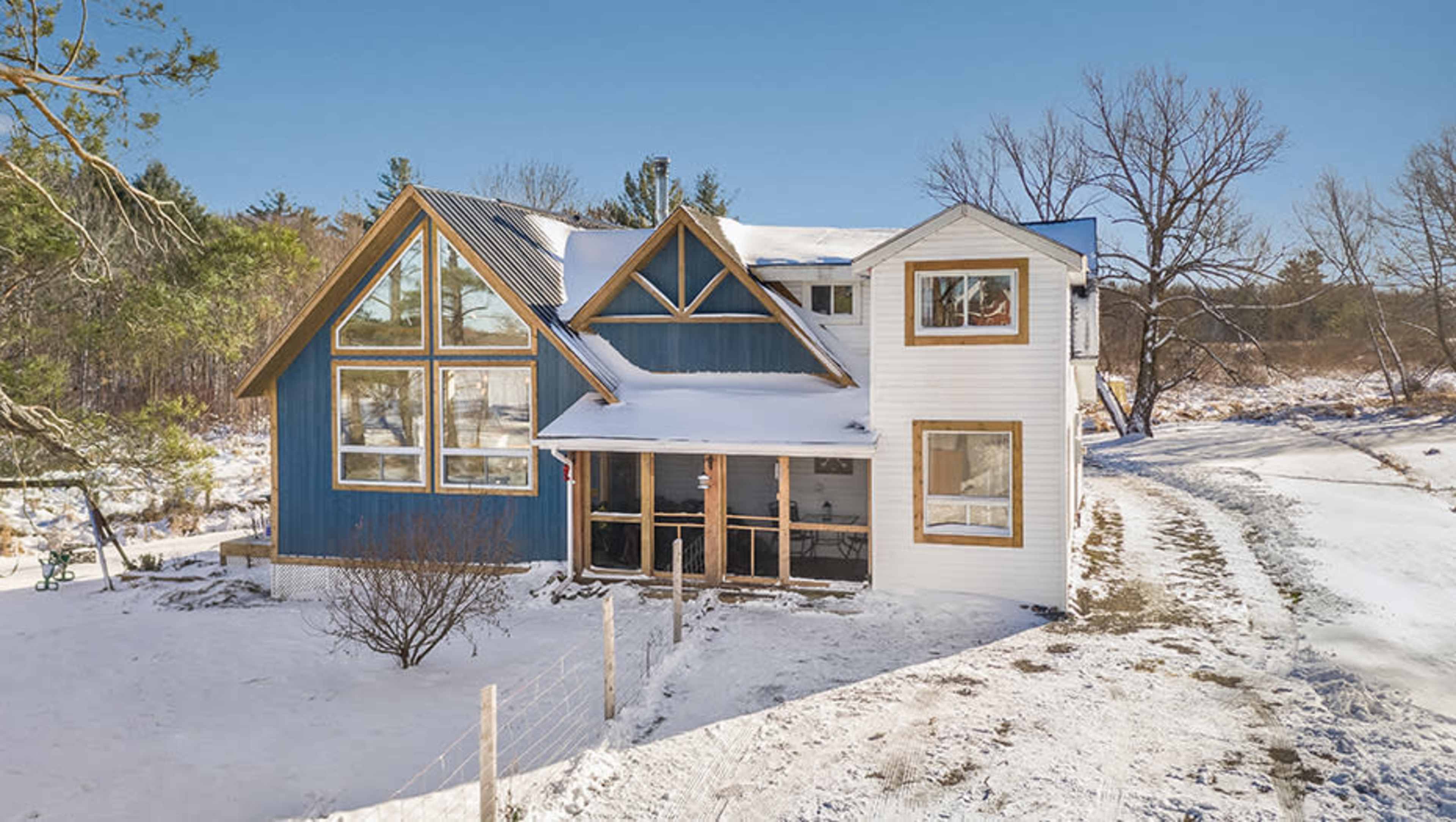 A modern two-story house with large windows is surrounded by snow on a clear winter day.