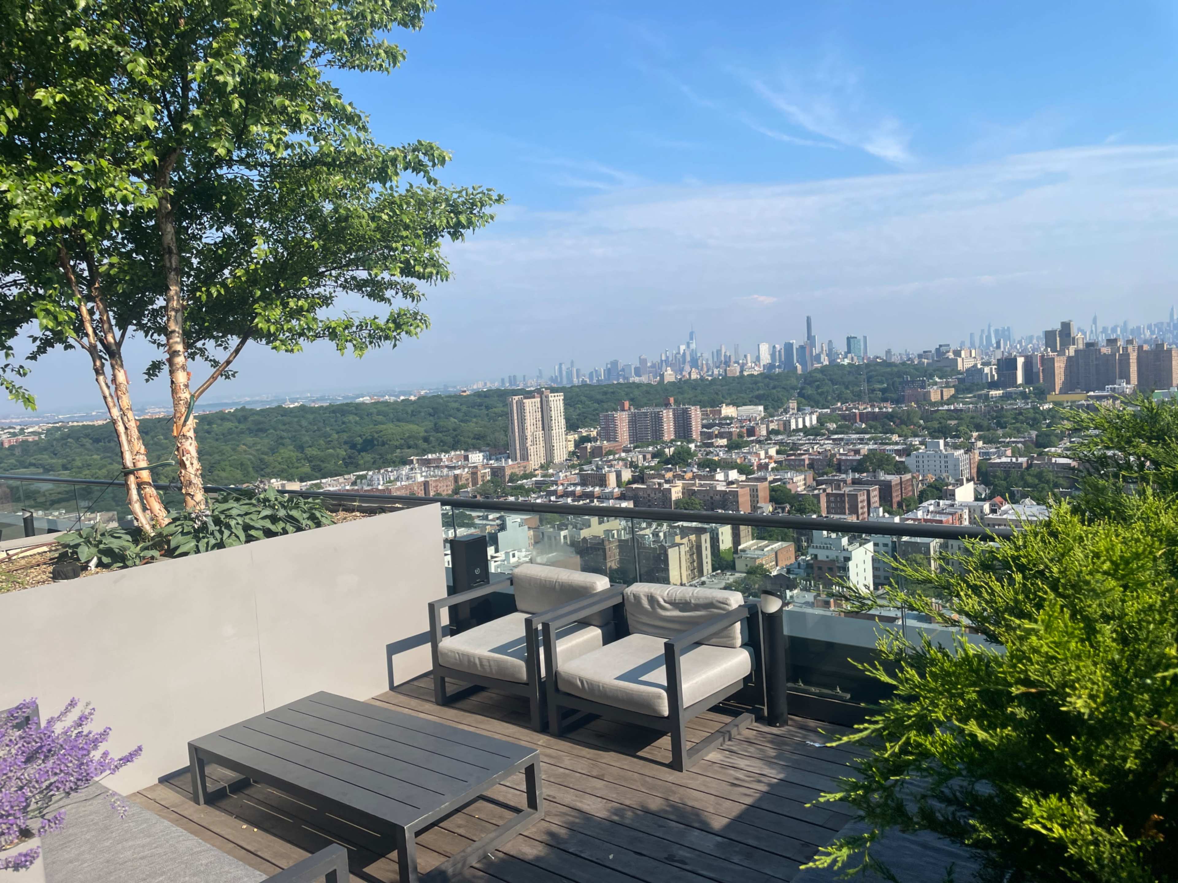 A rooftop terrace features modern seating and overlooks a city skyline with greenery in the foreground.