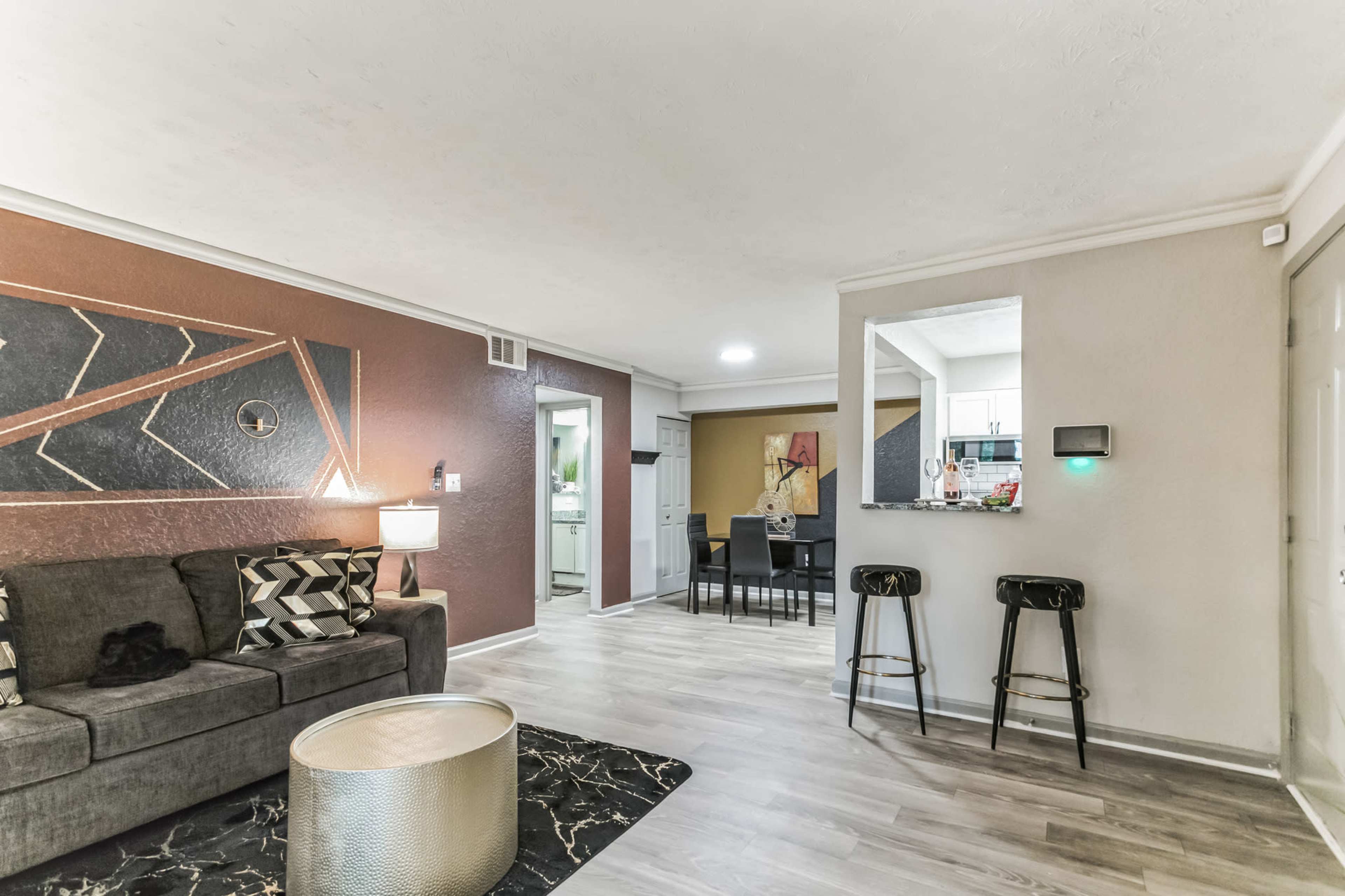 A modern living room with a sectional sofa, a round coffee table, and a view of a dining area and kitchen in the background.