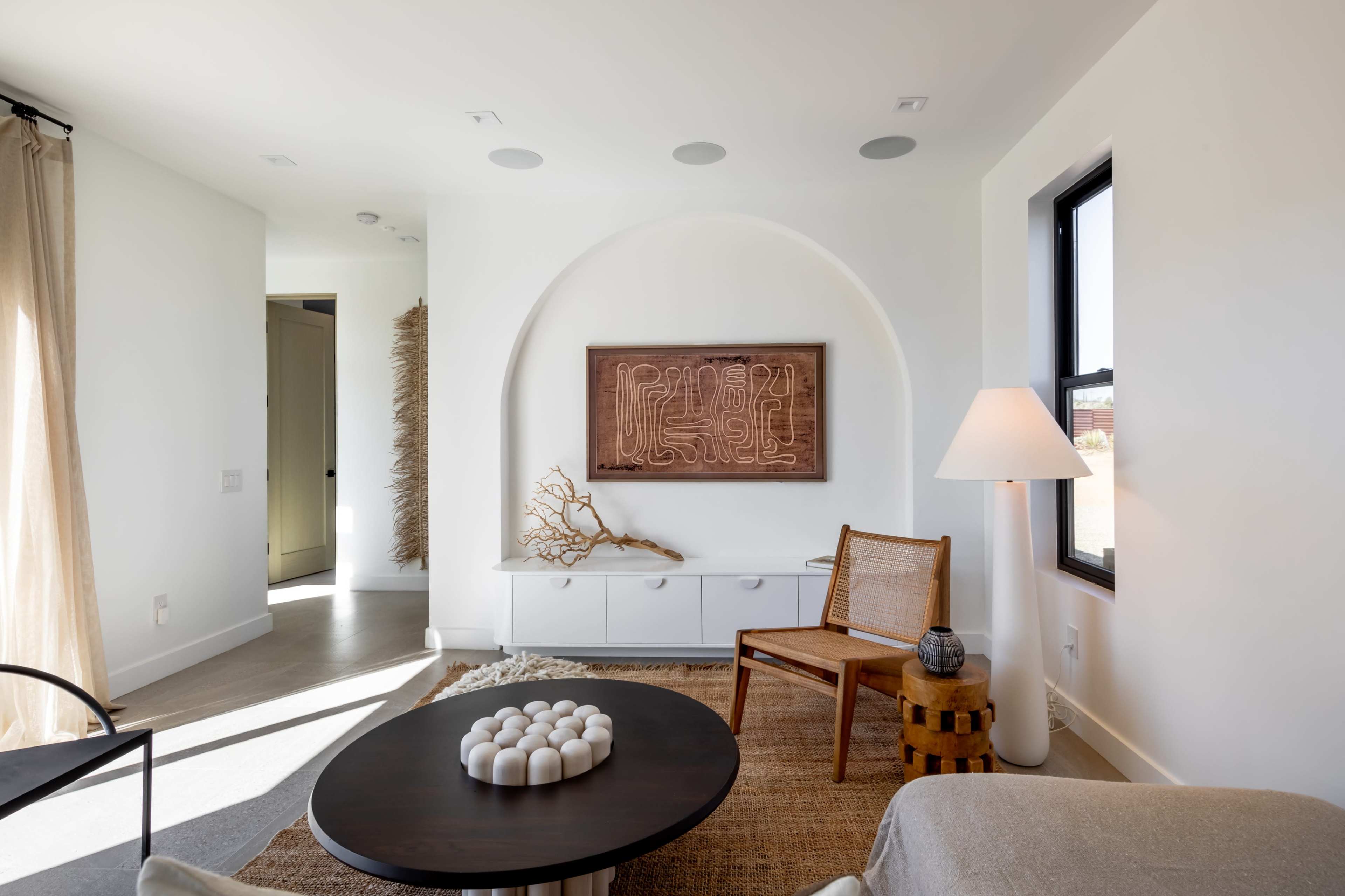 A modern living room featuring a wooden art piece on the wall, a round black coffee table, and a rattan chair beside a lamp.