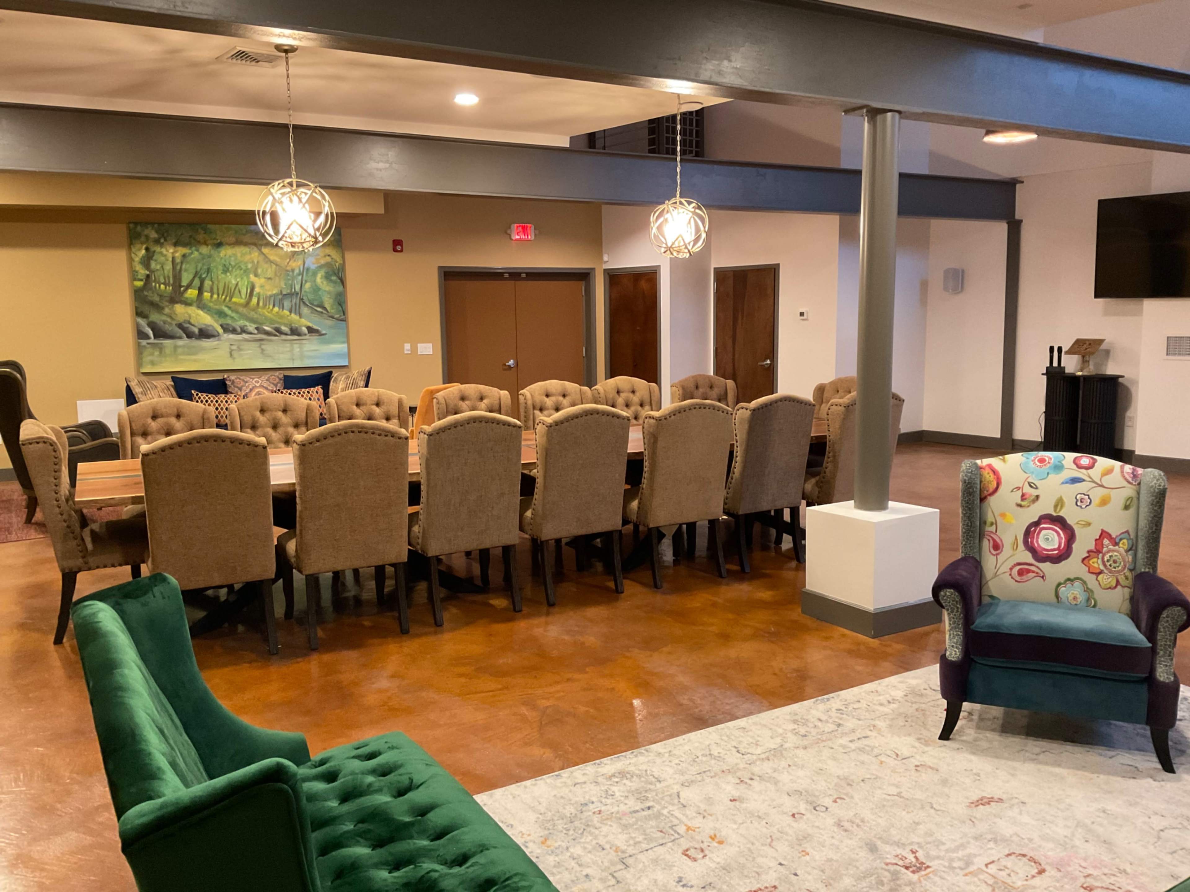 A spacious meeting room with a long wooden table surrounded by upholstered chairs, complemented by a colorful armchair and a decorative rug.