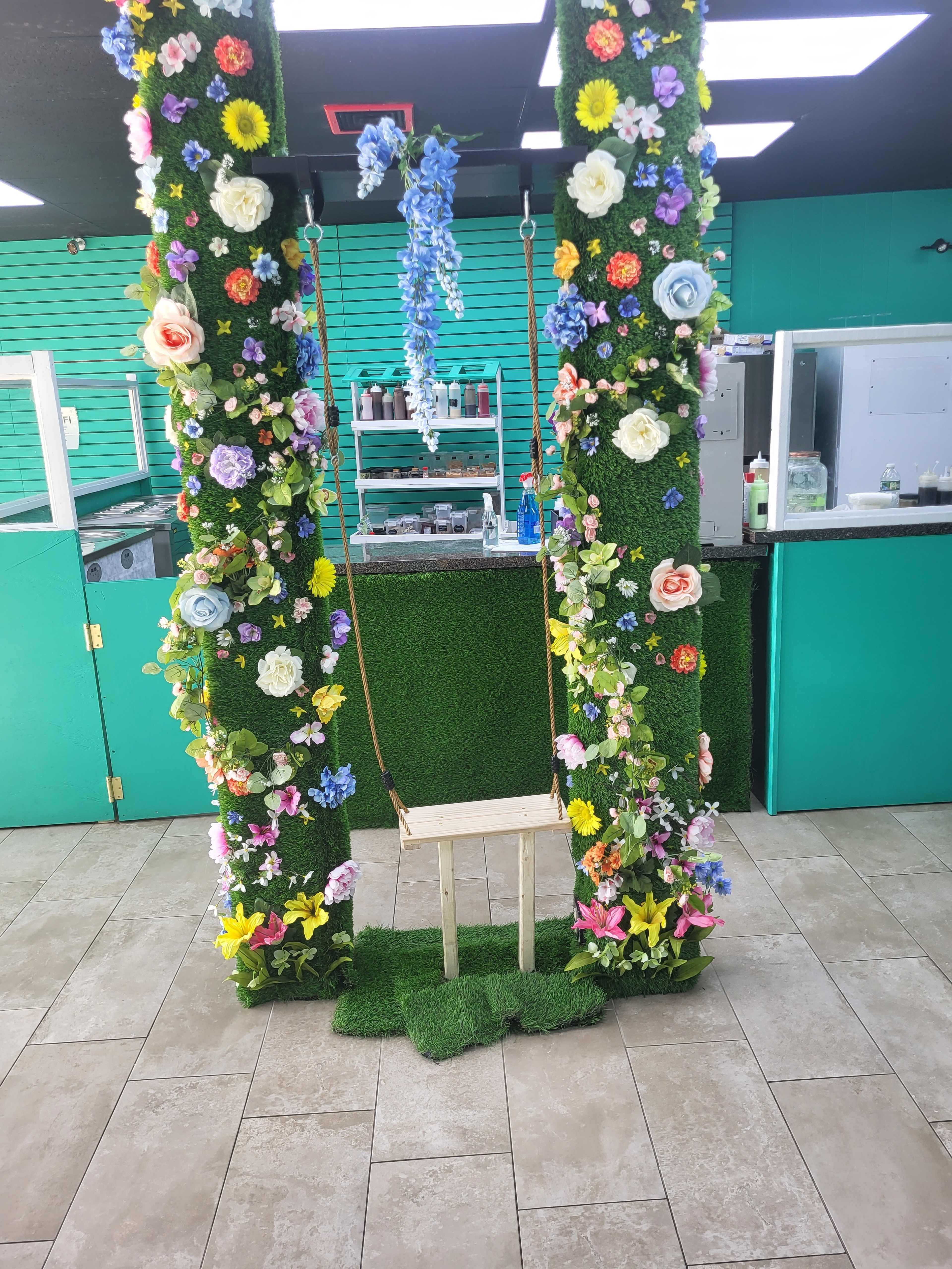 A decorative swing suspended between two green, flower-adorned columns in a brightly colored café or retail space.