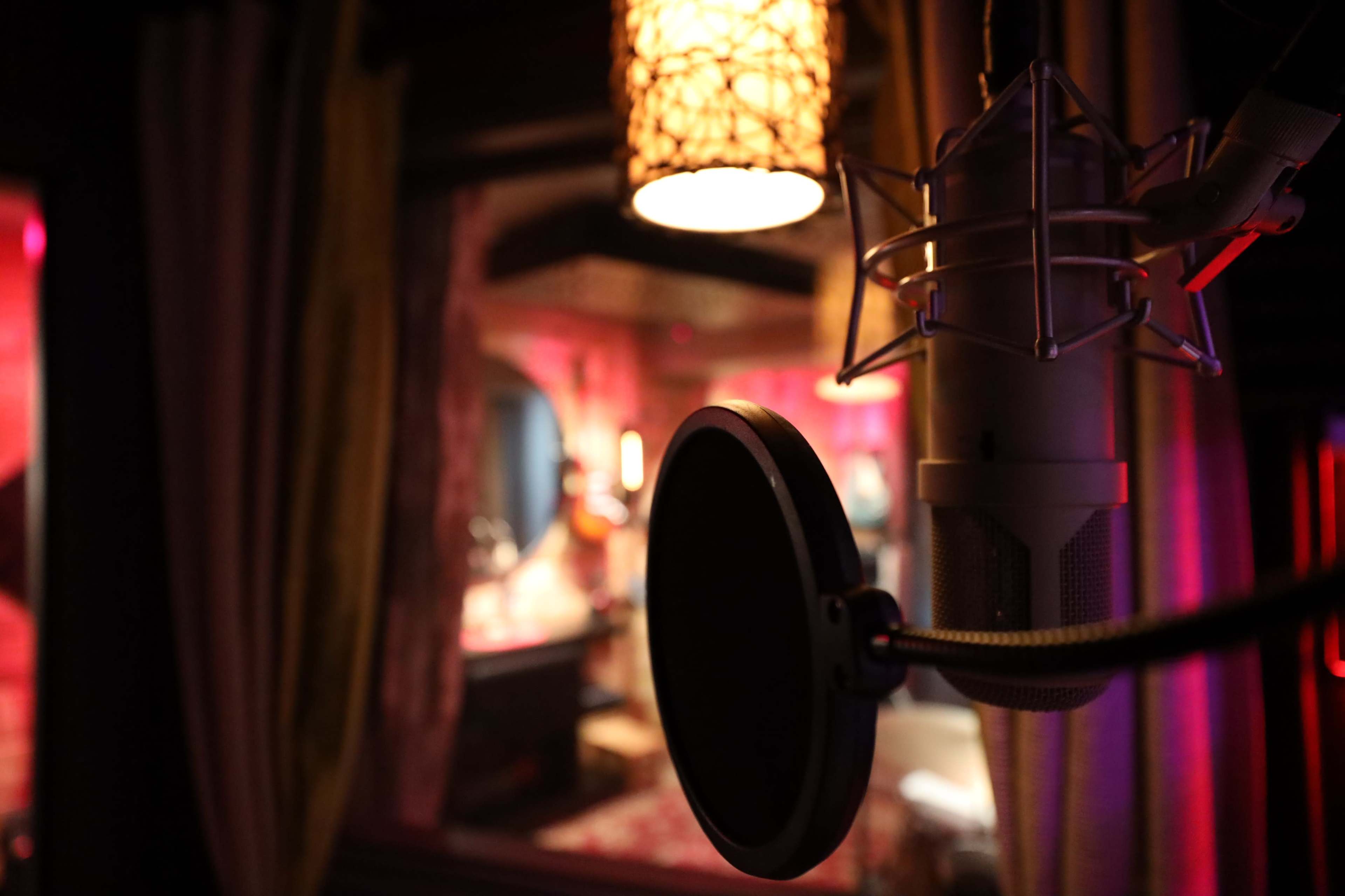 A microphone is positioned in the foreground with a softly illuminated recording studio visible in the background.