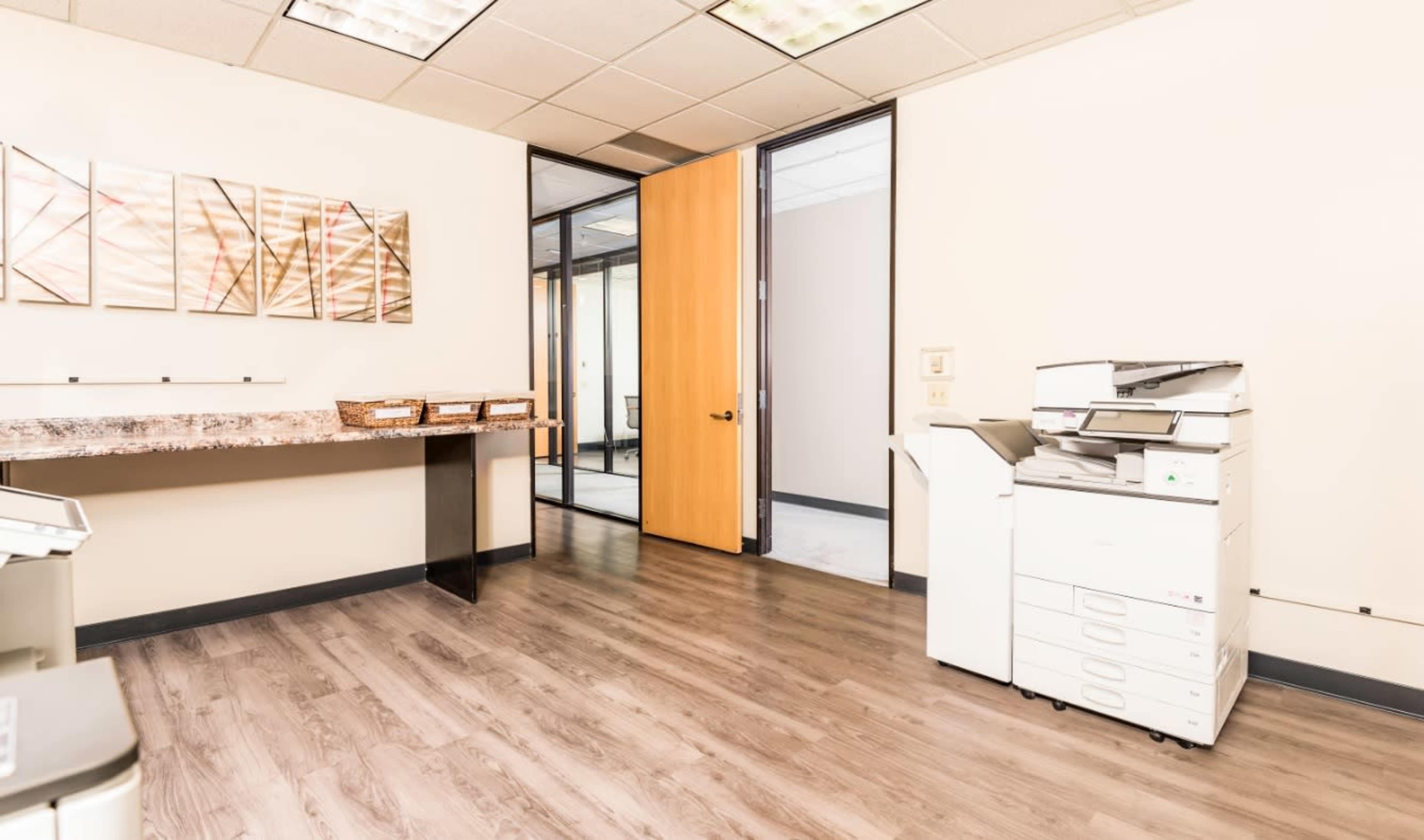 An office space features a wooden table against one wall, a doorway leading to another room, and a multifunction printer adjacent to it.
