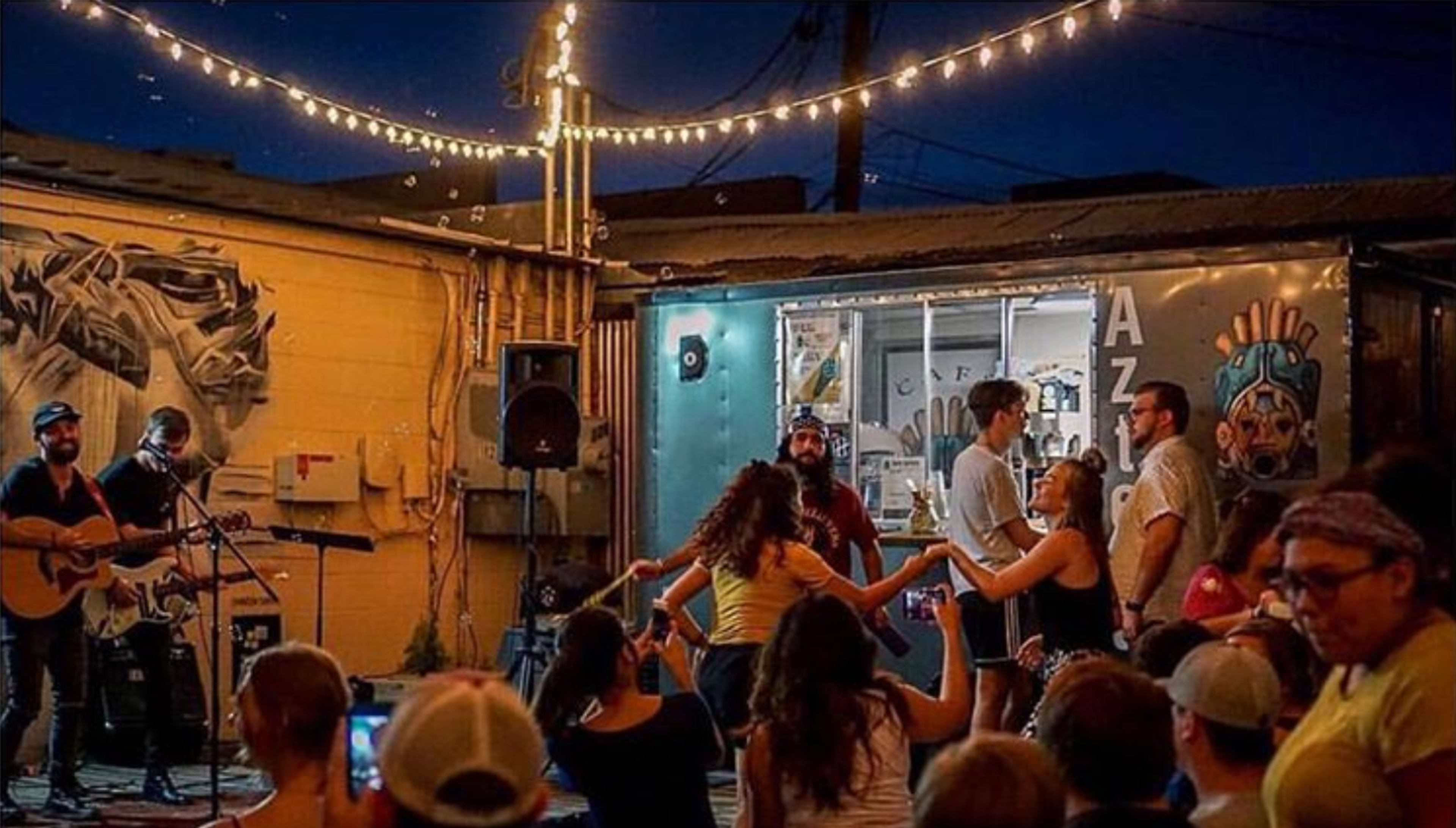 A live music event takes place outdoors, with a band performing on stage while people dance and enjoy the atmosphere.