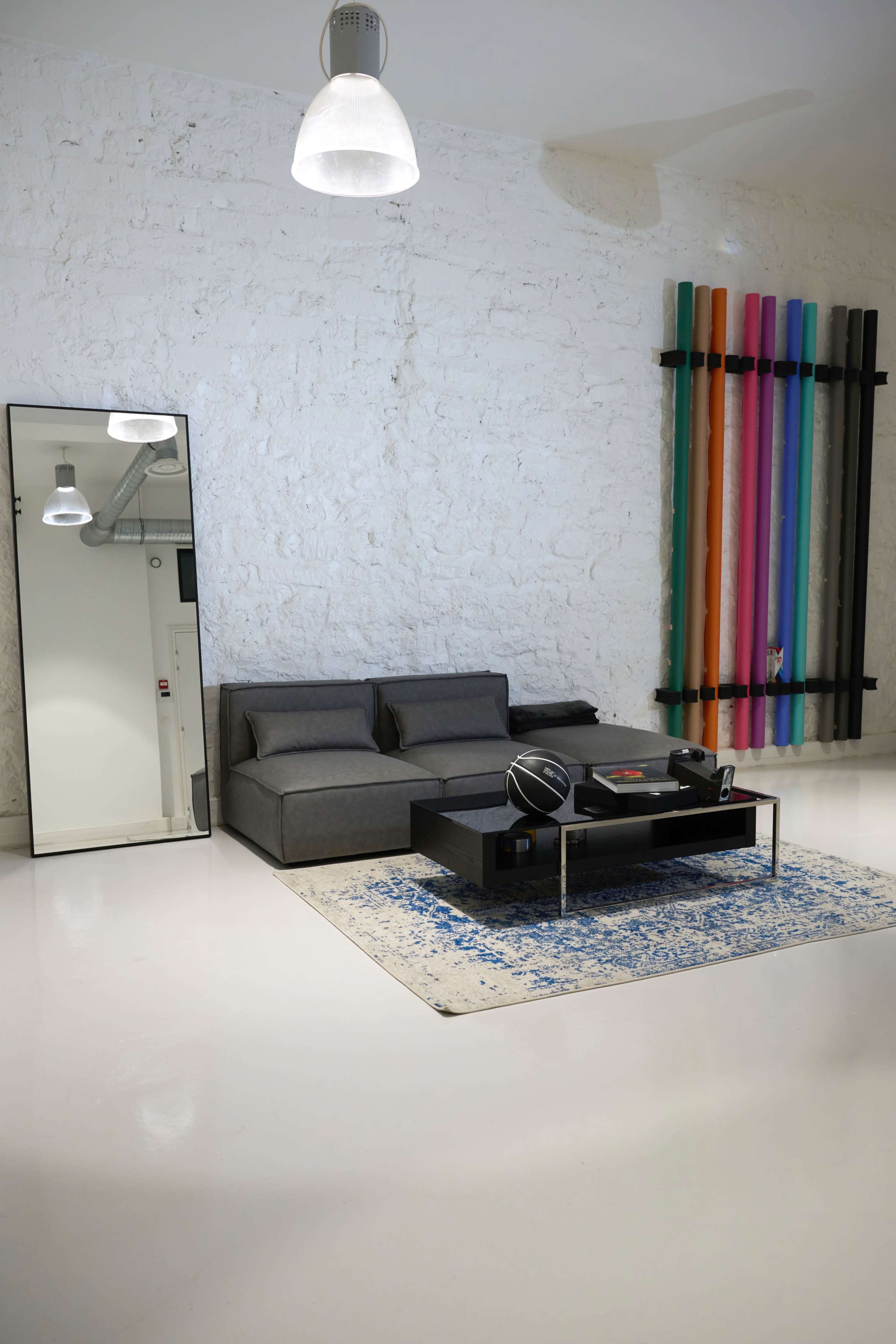 The room features a gray sofa, a low coffee table with a record player, a large mirror, and colorful vertical decorations against a white wall.