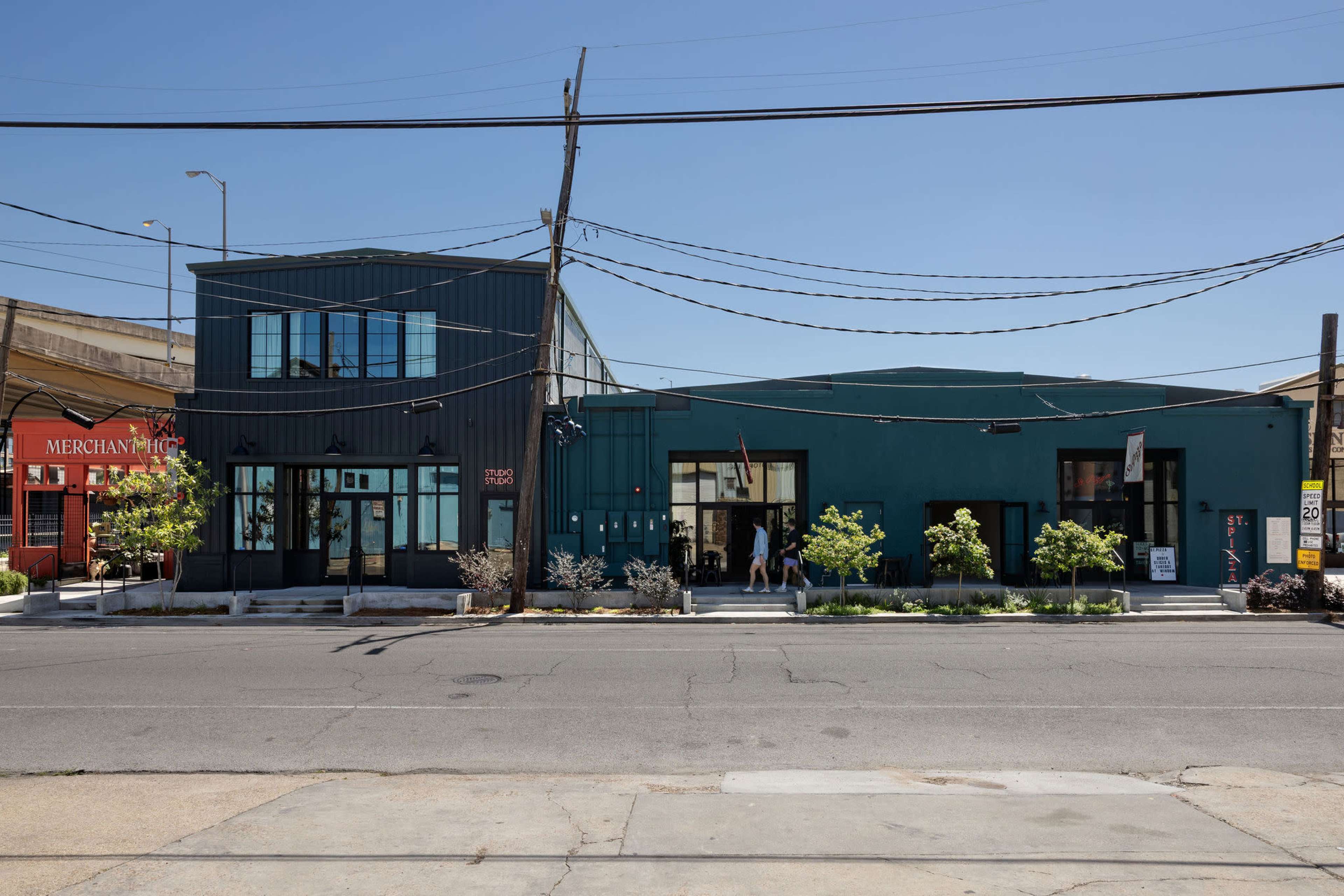 The image shows a modern building with a dark facade and large windows, situated across the street from a bright red structure labeled "Merchant."