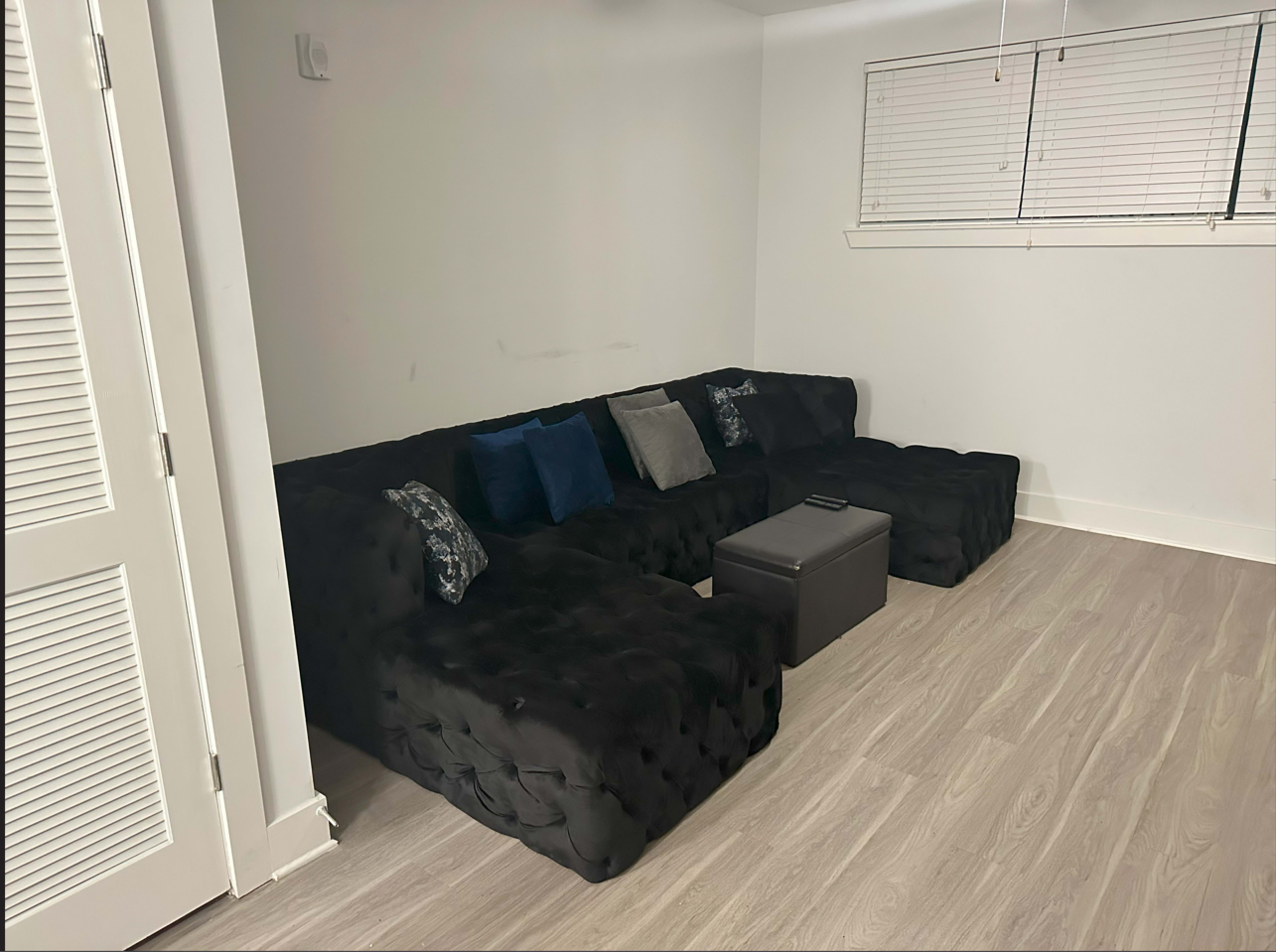 A semi-furnished room features a black sectional sofa with decorative pillows and a small black table in front of it.