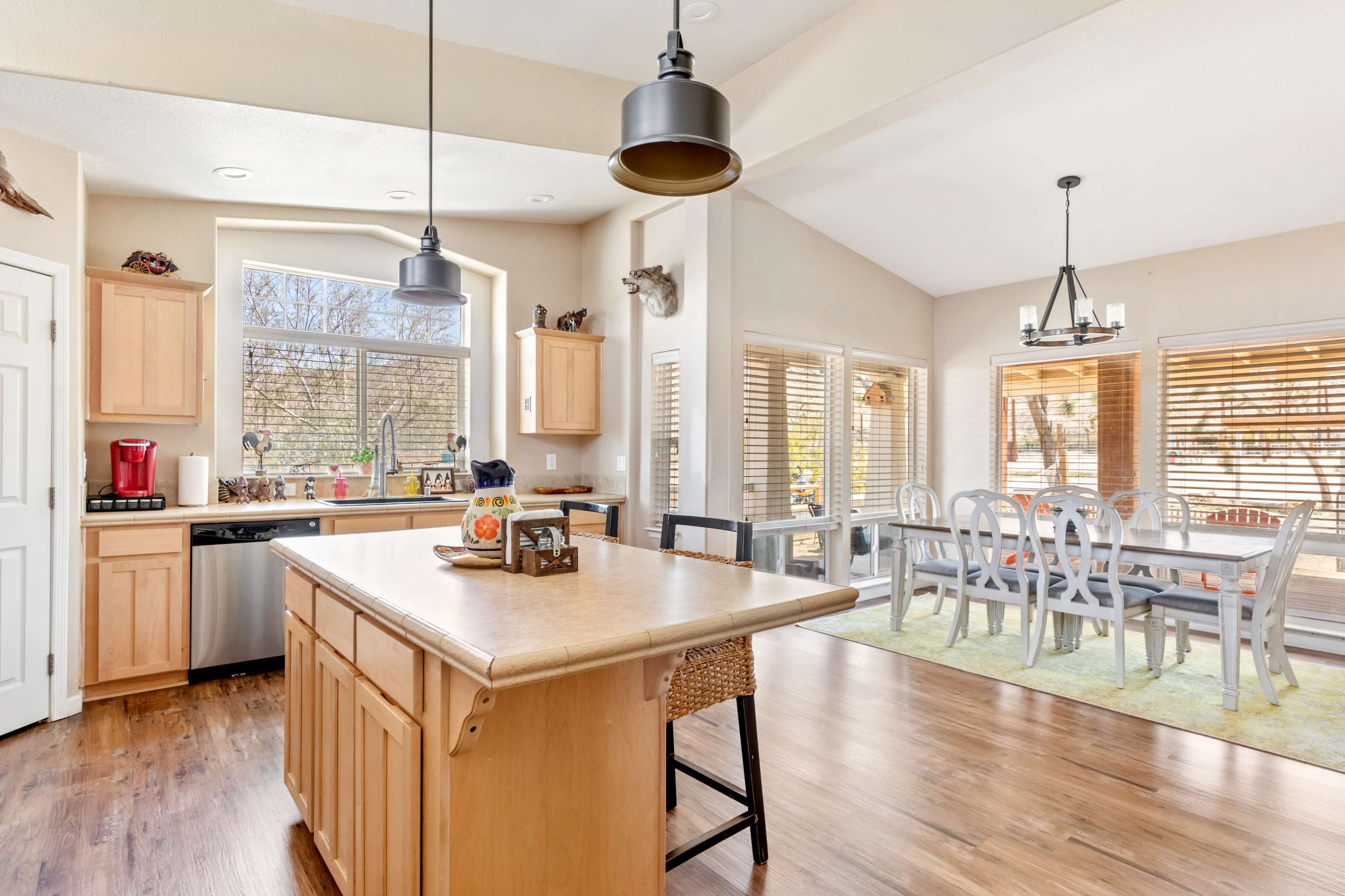 A spacious kitchen with wooden cabinets, a central island, and a dining area featuring large windows and a table set for several people.