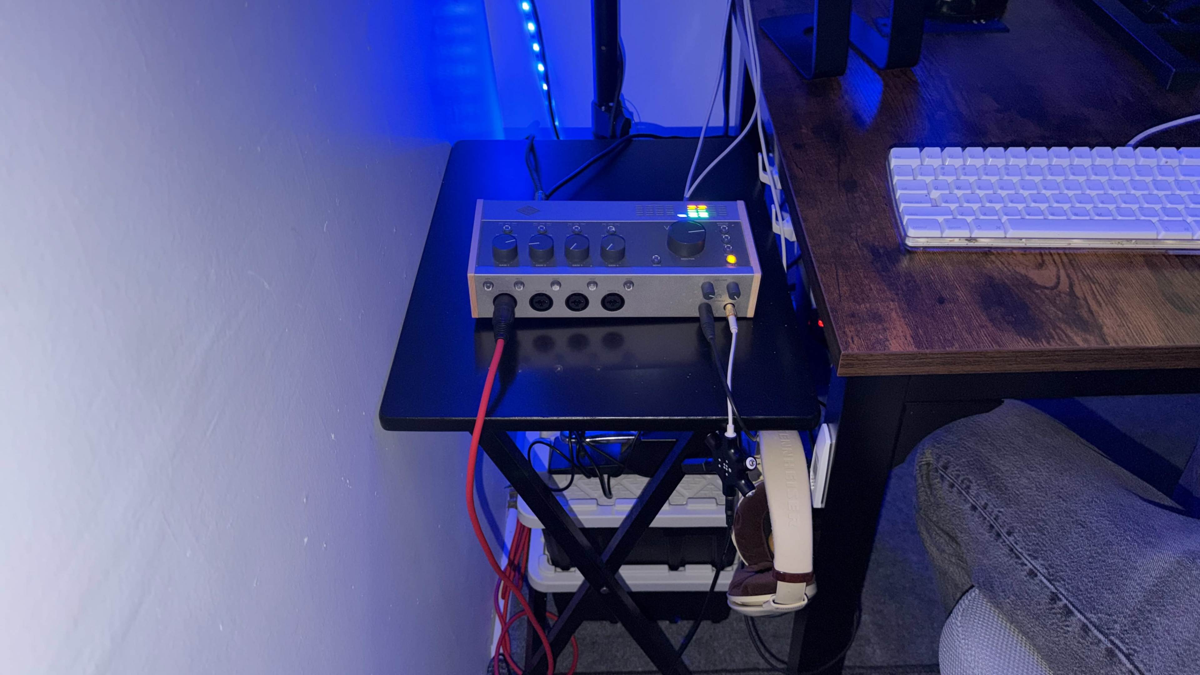 A silver audio interface is positioned on a small black table, connected to a computer keyboard and other cables, with ambient blue lighting in the background.