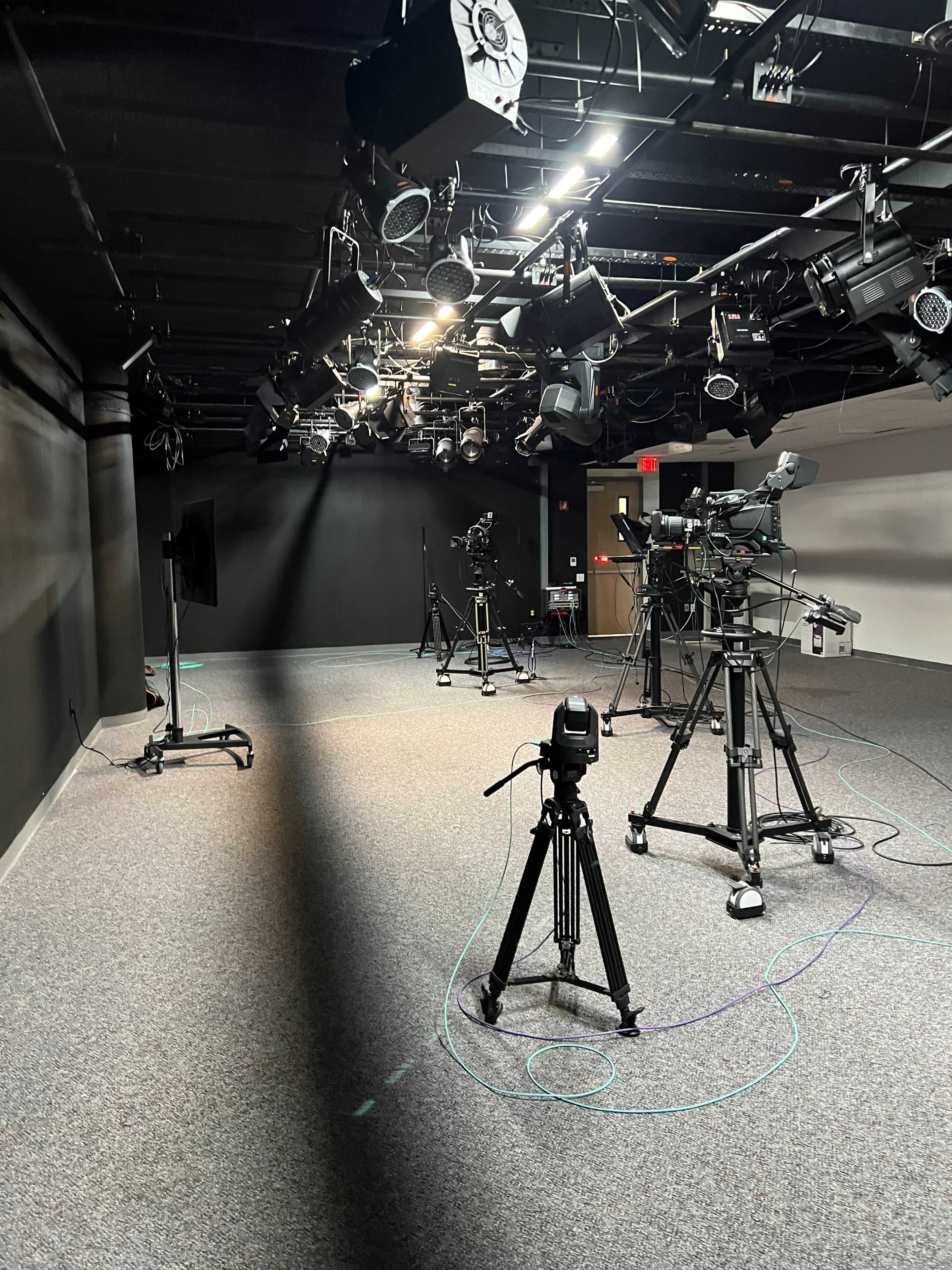 The image shows a well-lit studio space equipped with multiple cameras and lighting equipment set up on tripods.