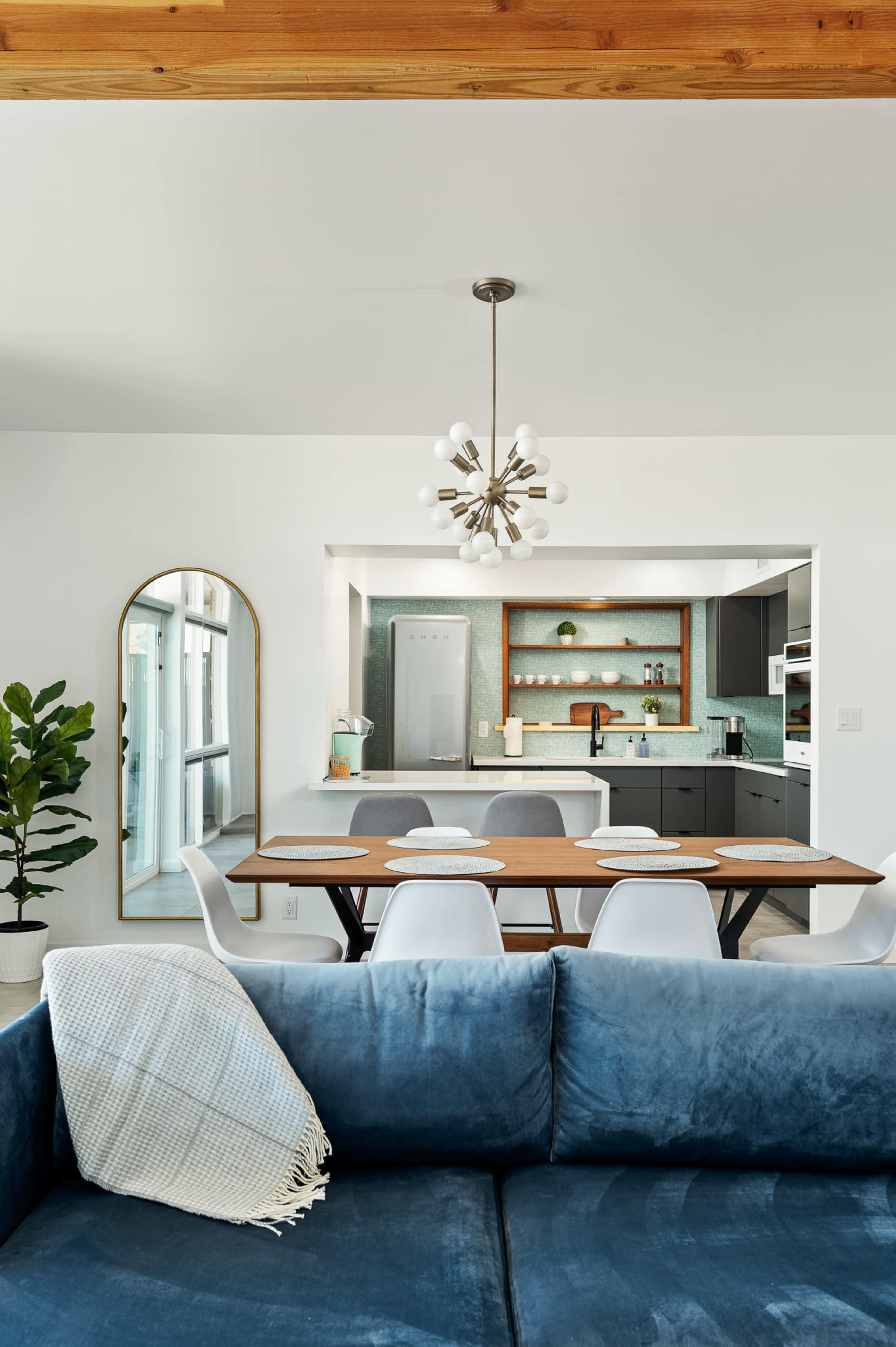 A modern dining area features a wooden table surrounded by chairs, with a kitchen visible in the background.