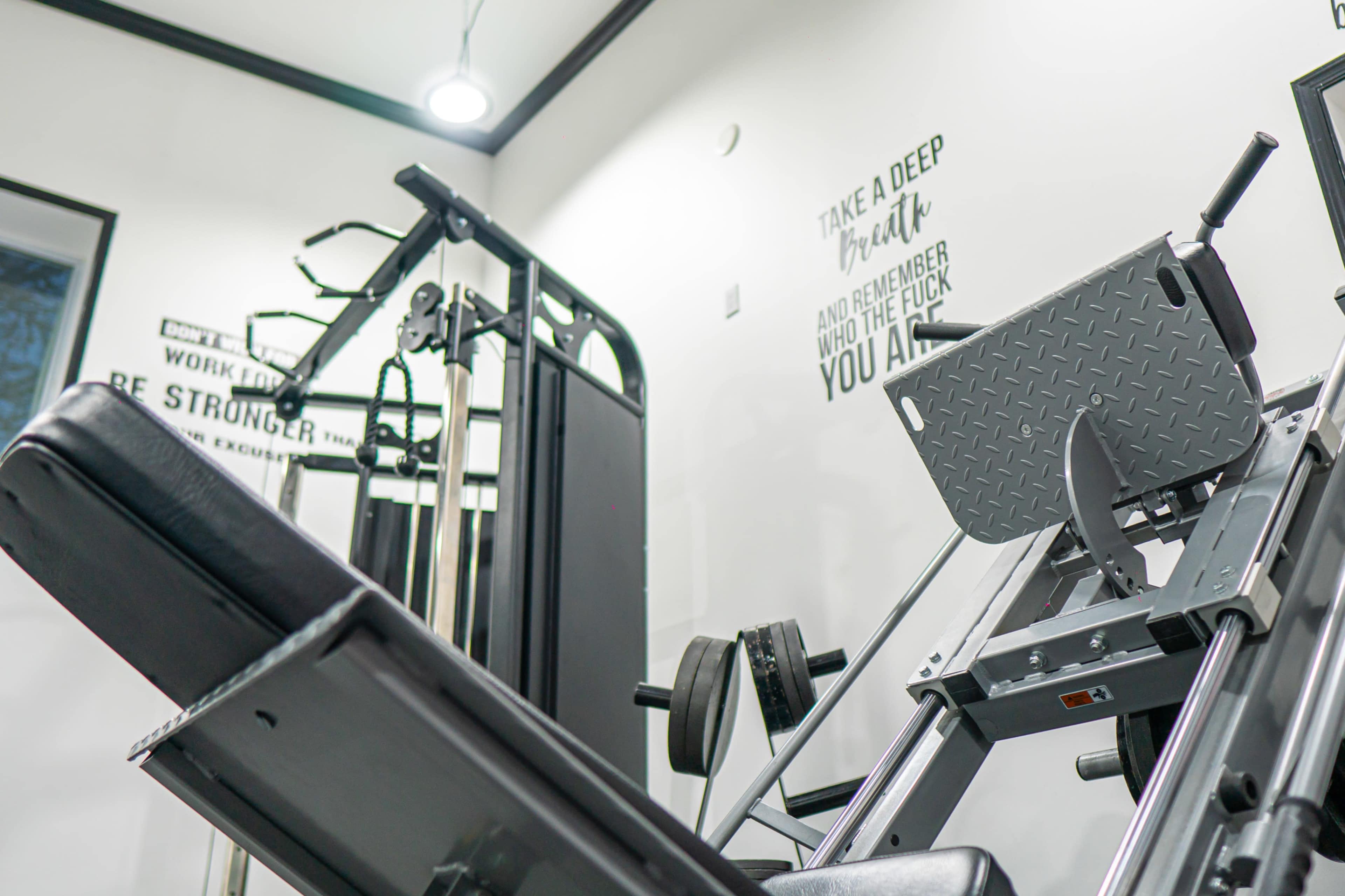A well-equipped home gym with various exercise machines and equipment against a white wall featuring motivational text.
