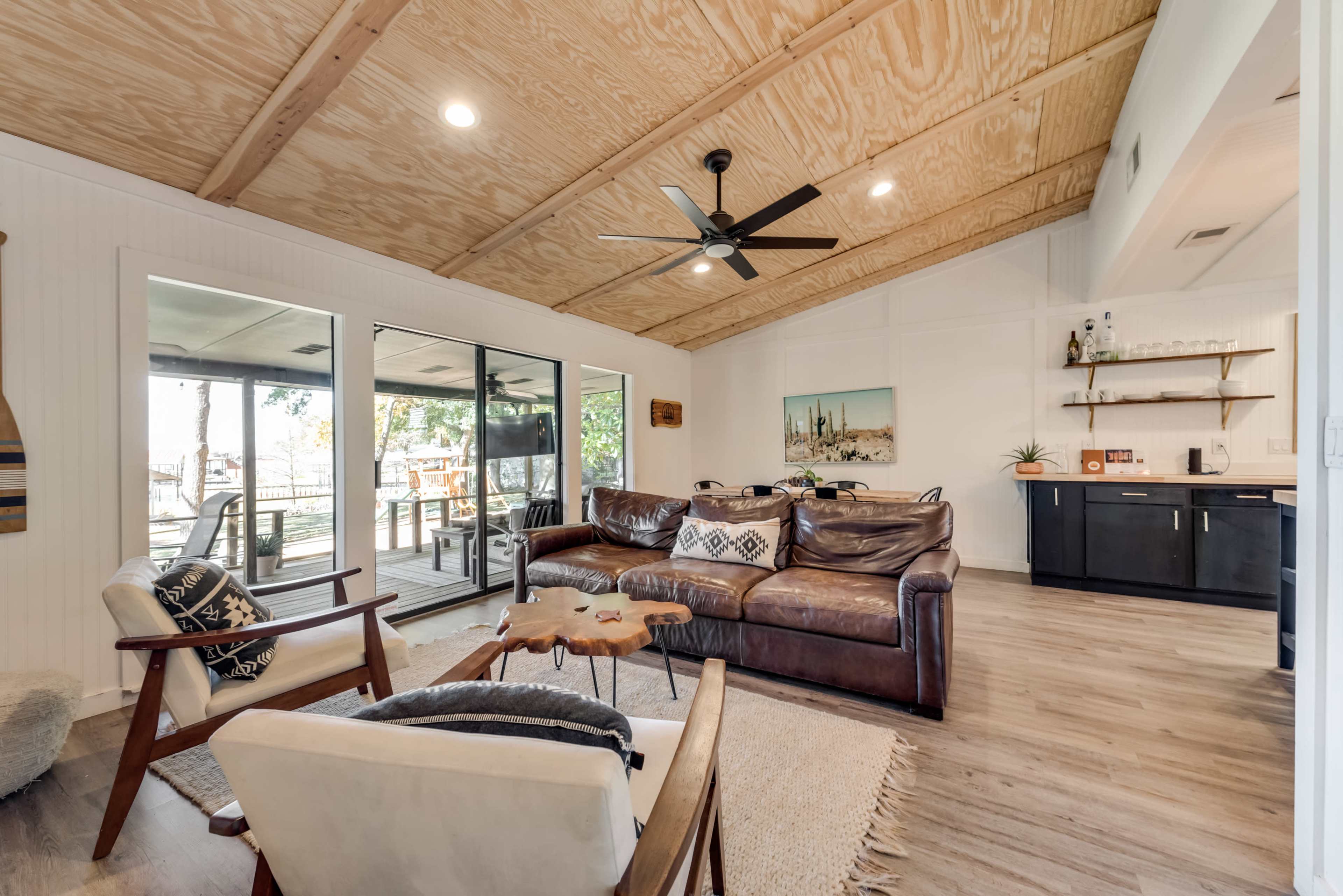 The living room features a leather sectional sofa, a wooden coffee table, and large sliding glass doors that lead to an outdoor deck.
