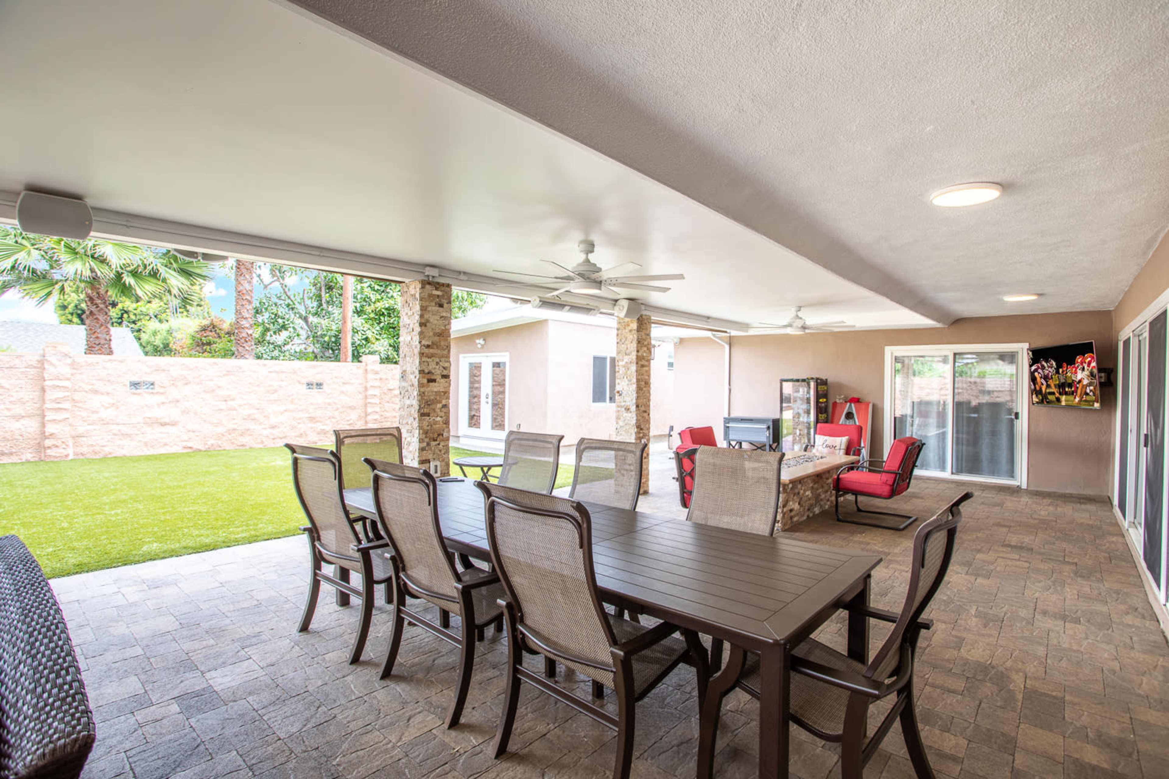 A covered outdoor patio featuring a large dining table with chairs, ceiling fans, and an entertainment area with a television.