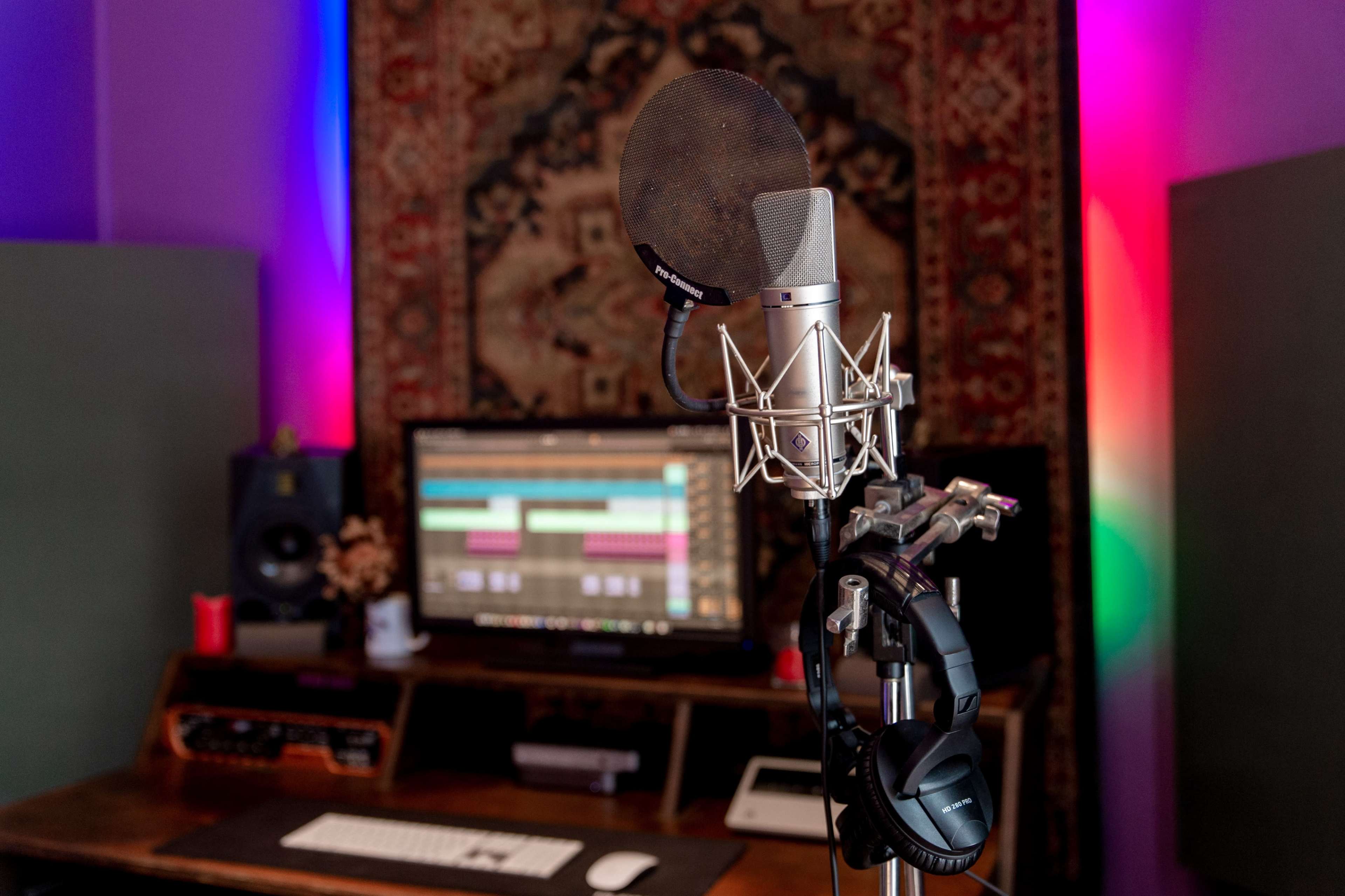 A microphone is positioned in front of a computer monitor displaying audio editing software in a recording studio.