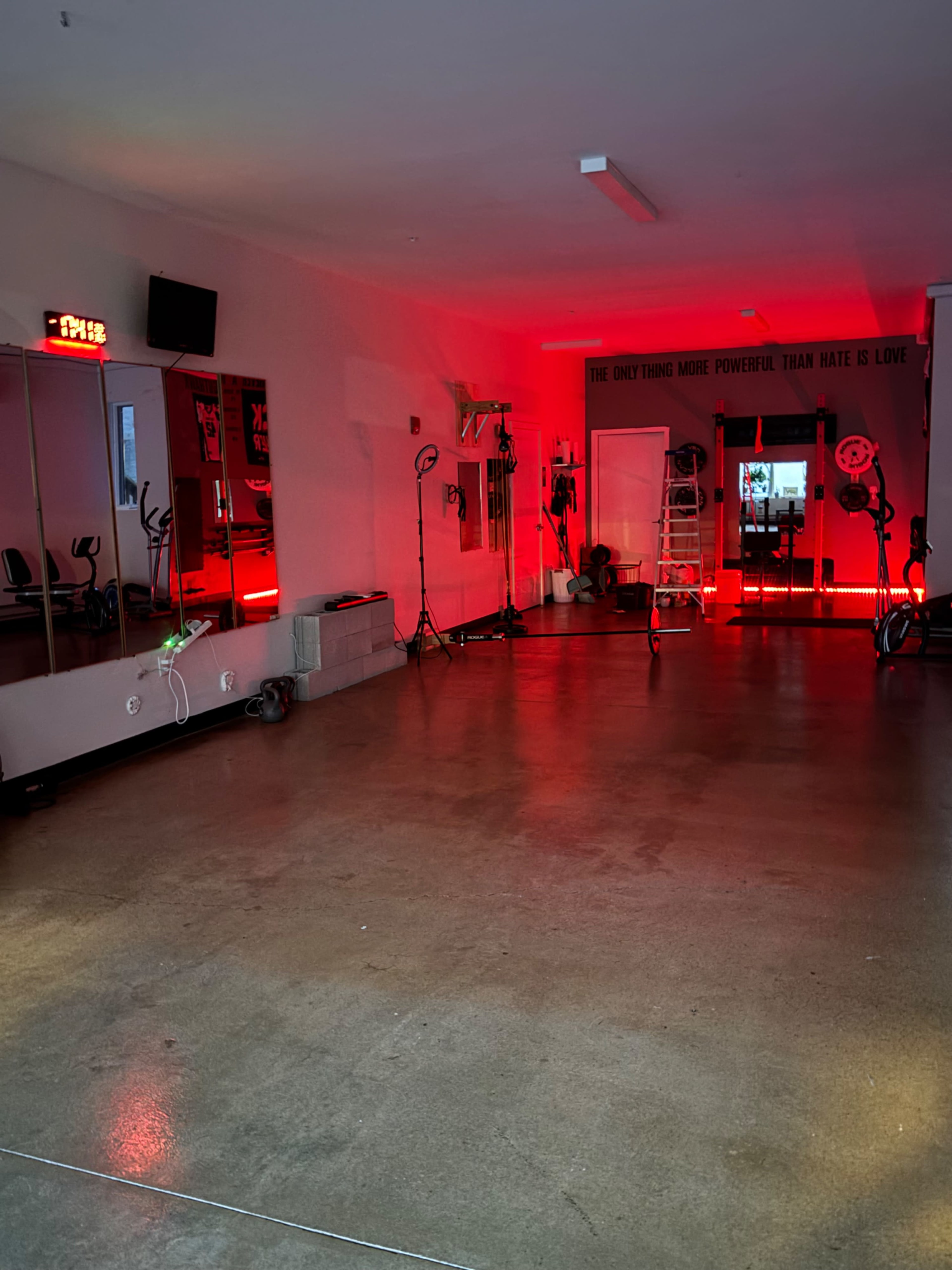 The image shows an empty gym with red lighting, a large mirror, and exercise equipment arranged around the space.