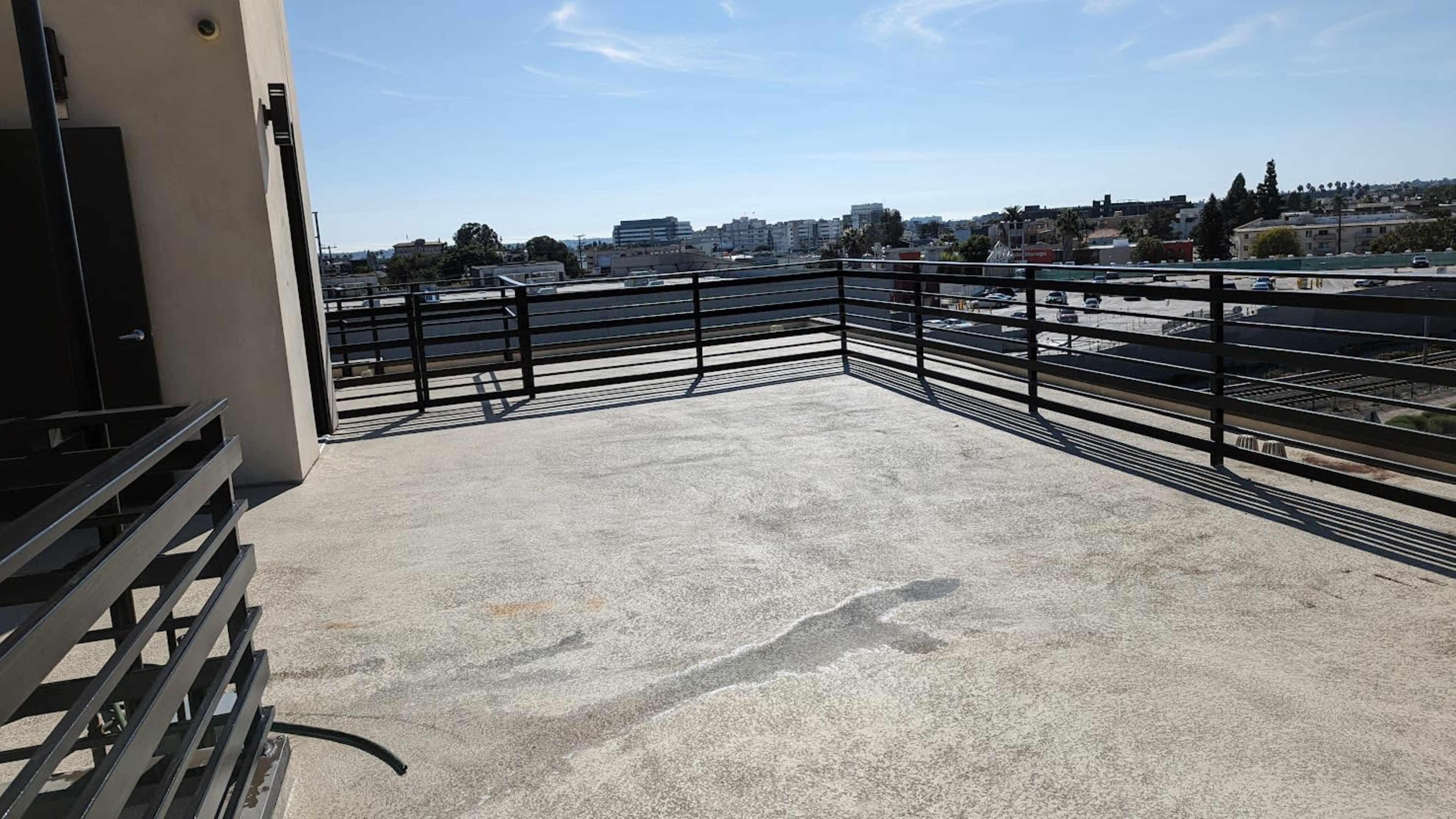 The image shows a spacious balcony with a clear view of buildings and a highway in the background under a bright blue sky.