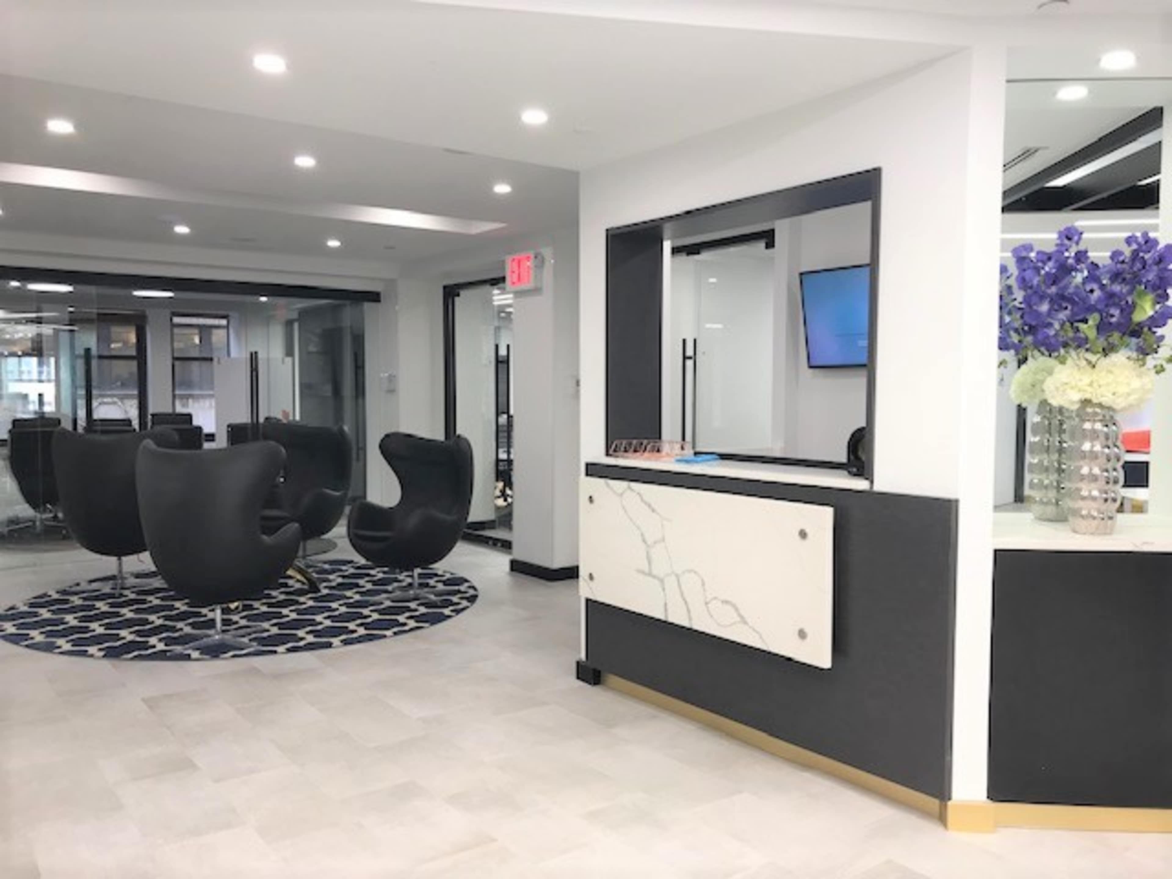 The image shows a modern reception area with a white desk, black seating chairs, and a circular blue patterned rug.