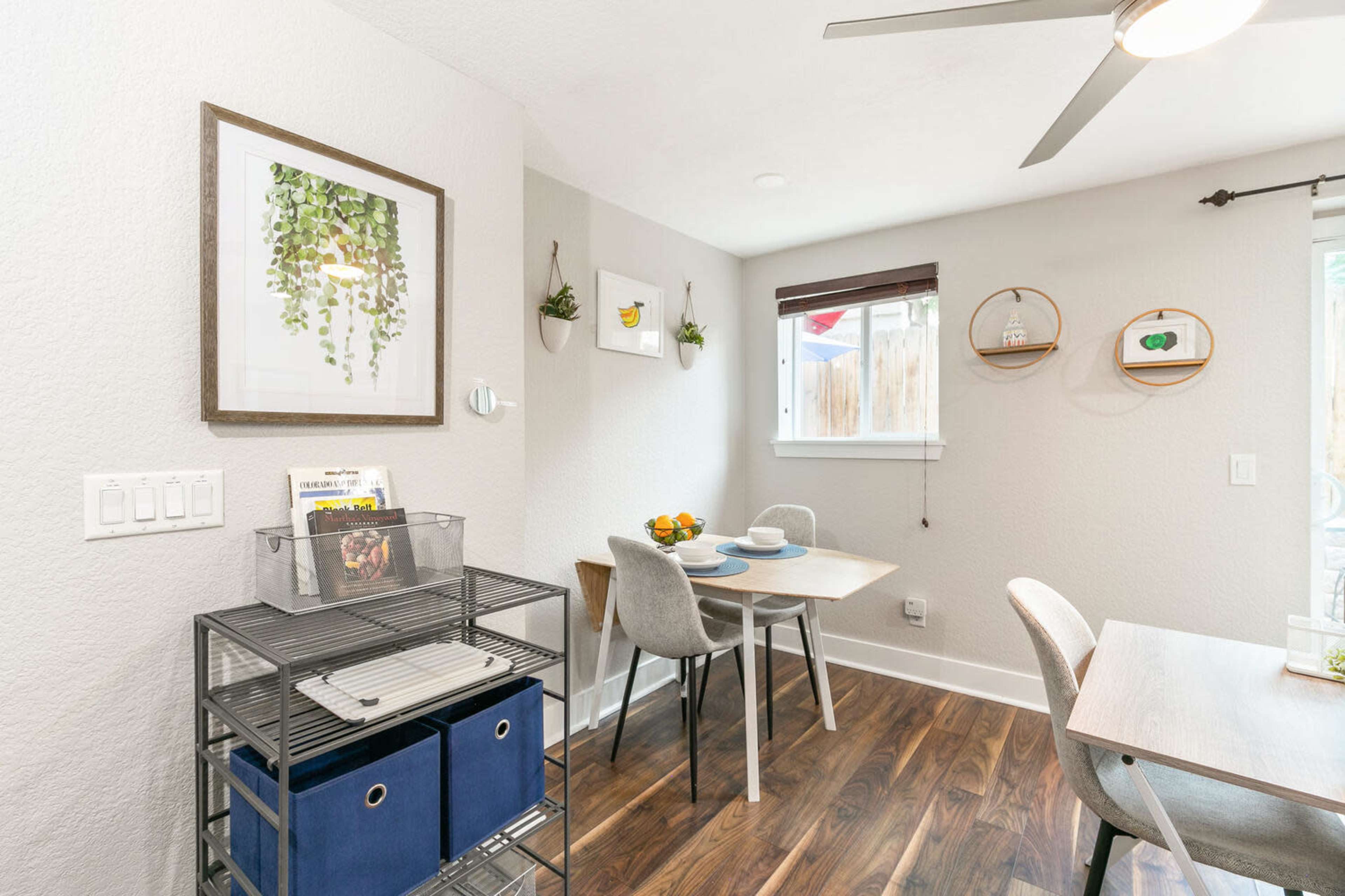 The image features a modern dining area with a small table set for two, a wall-mounted shelf, and a ceiling fan.