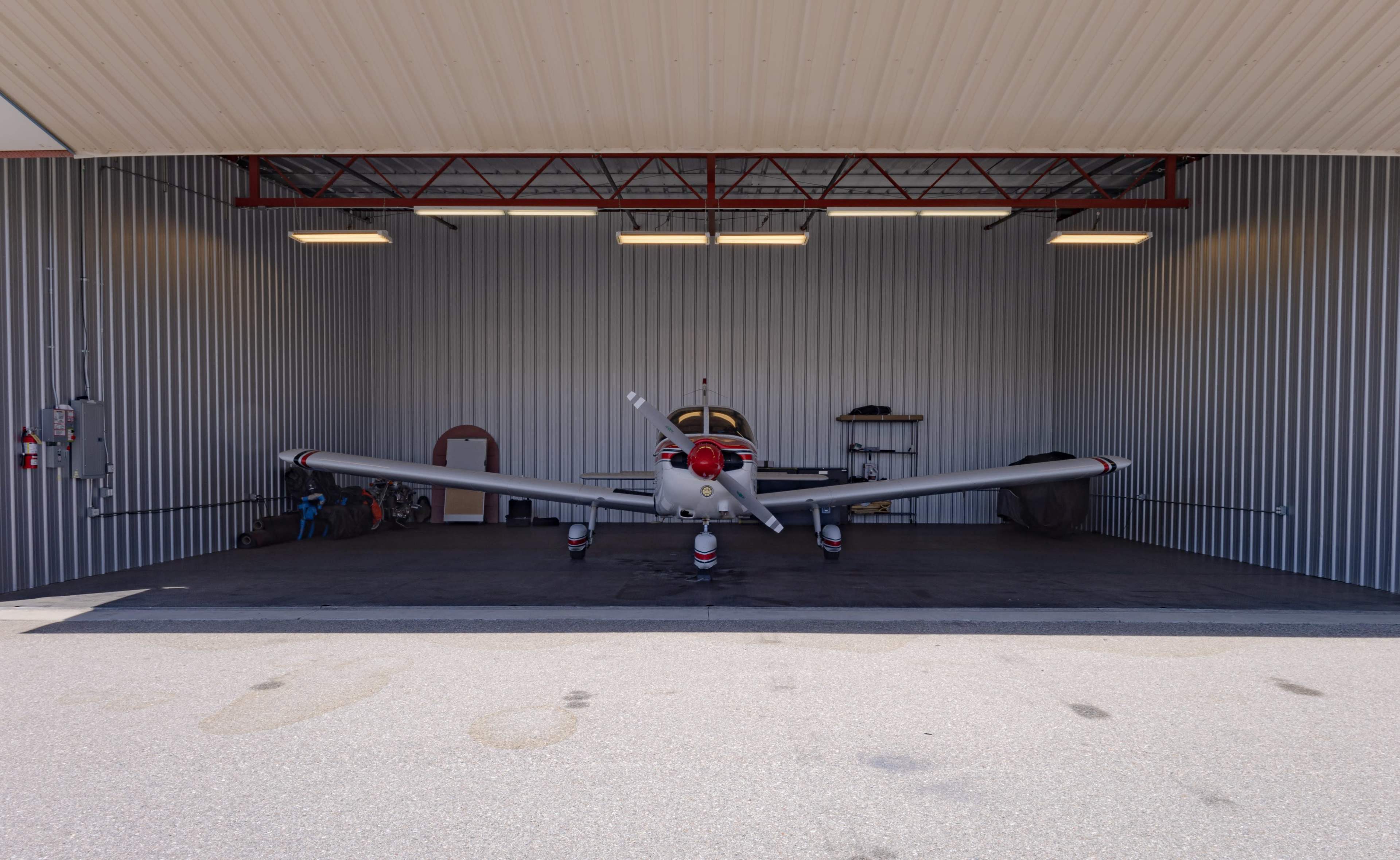 A small aircraft is parked inside a hangar with metal walls and bright overhead lighting.