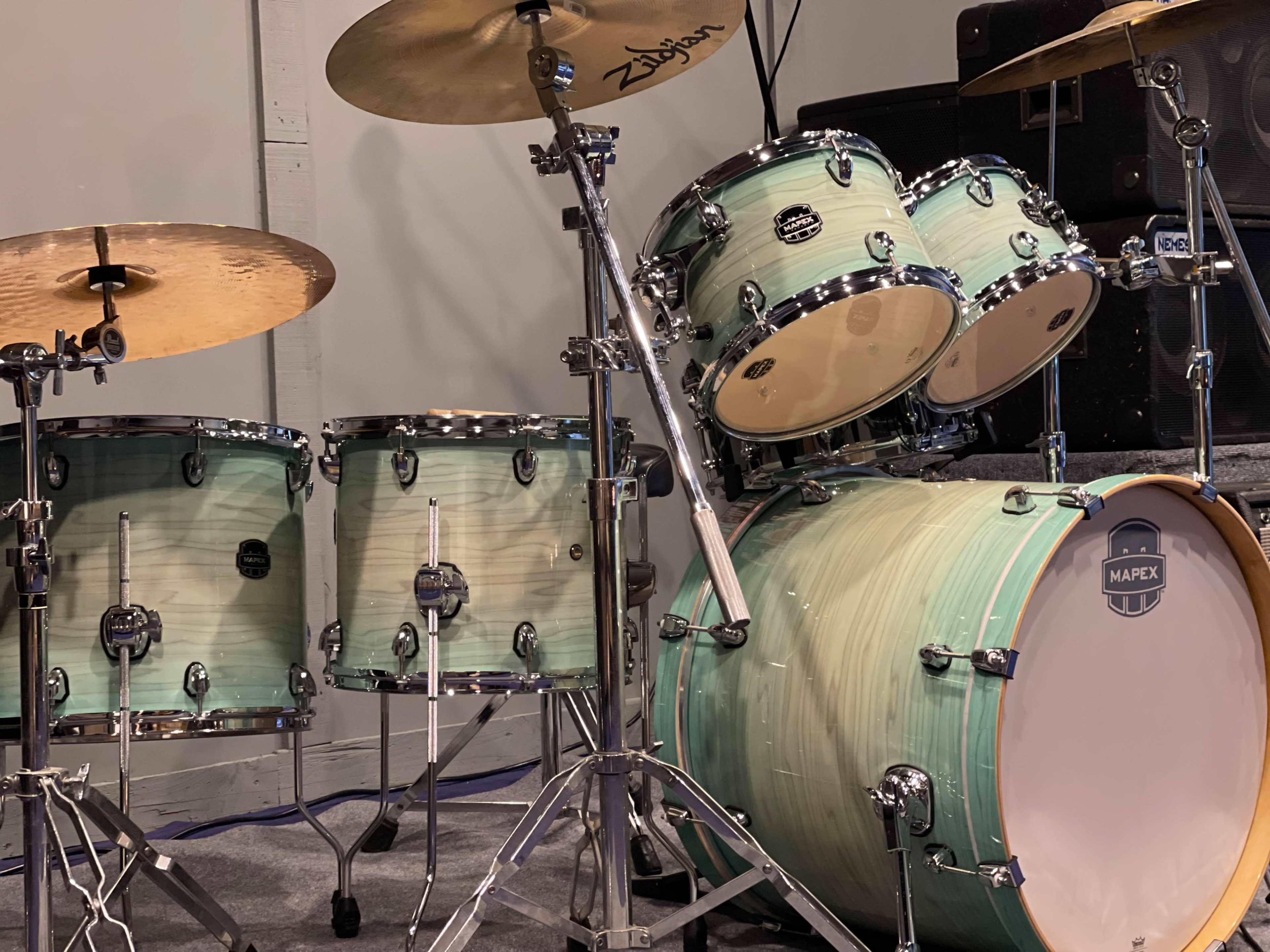 A set of acoustic drums with a light green finish, accompanied by cymbals and equipment in a music rehearsal space.