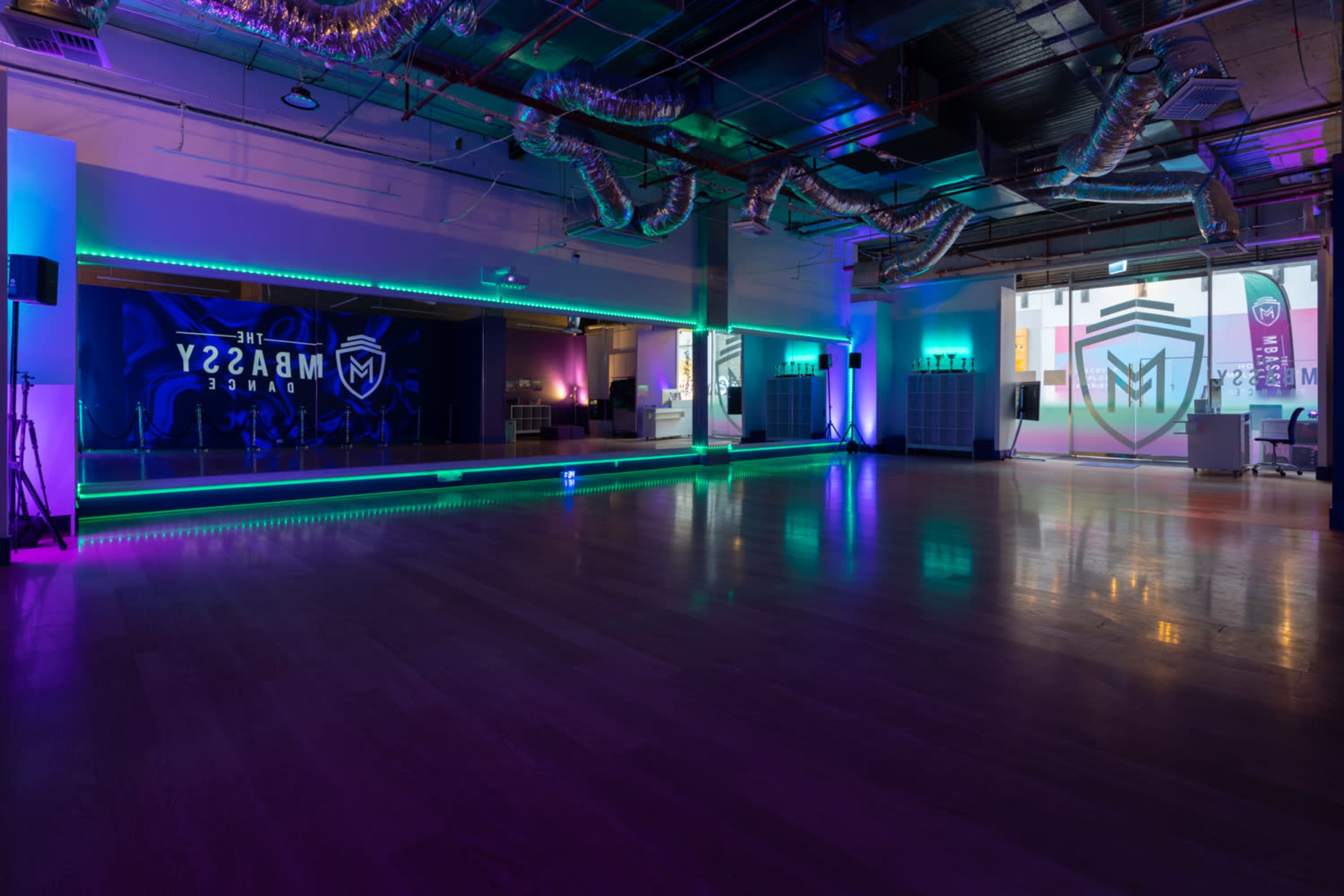 A spacious, modern dance studio with illuminated walls and a polished wooden floor, featuring colorful LED lighting.