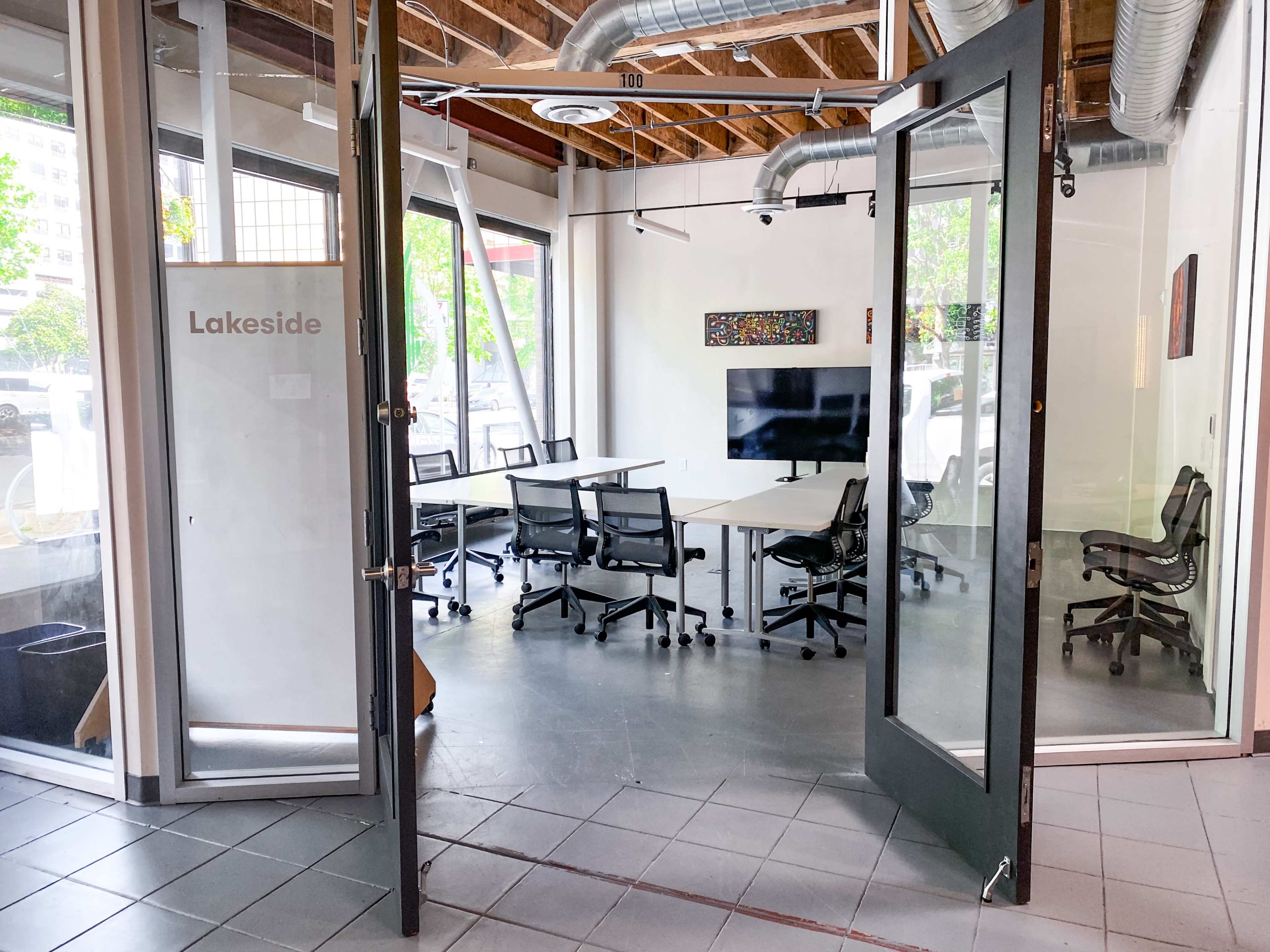 A modern meeting room with glass doors, equipped with a table, chairs, and a wall-mounted television.