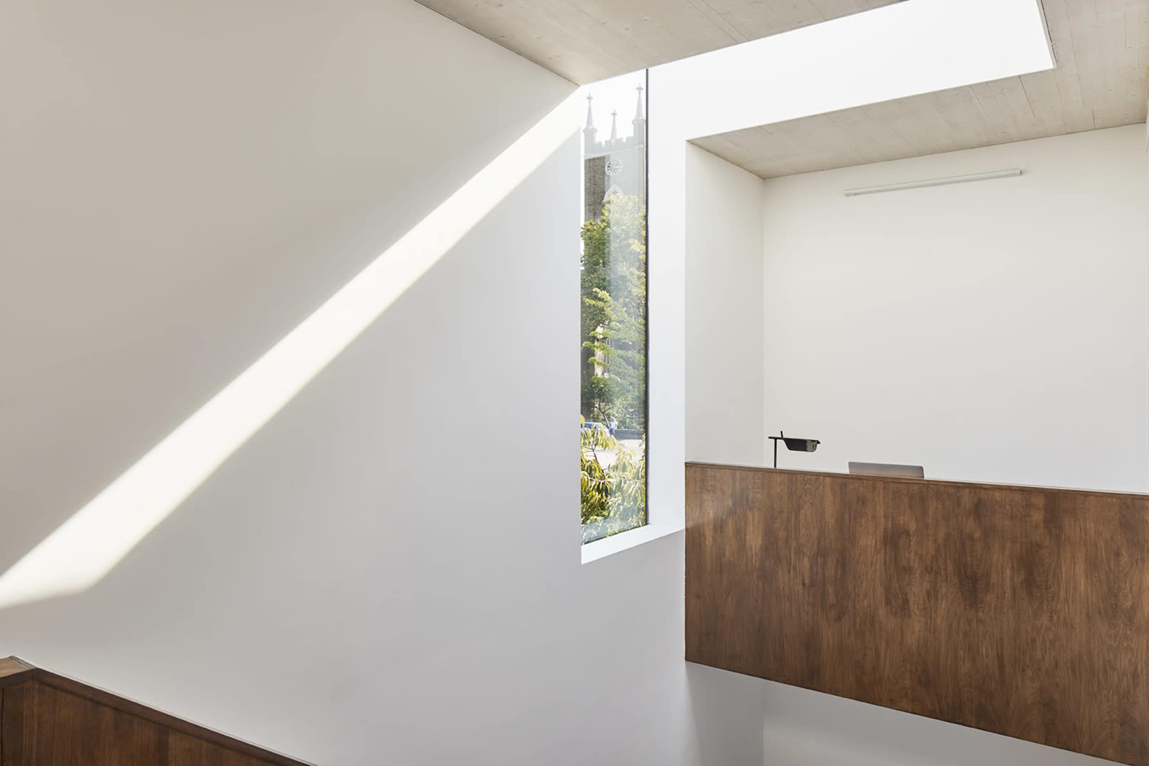 A modern interior space featuring a wooden railing and a large window that lets in natural light.
