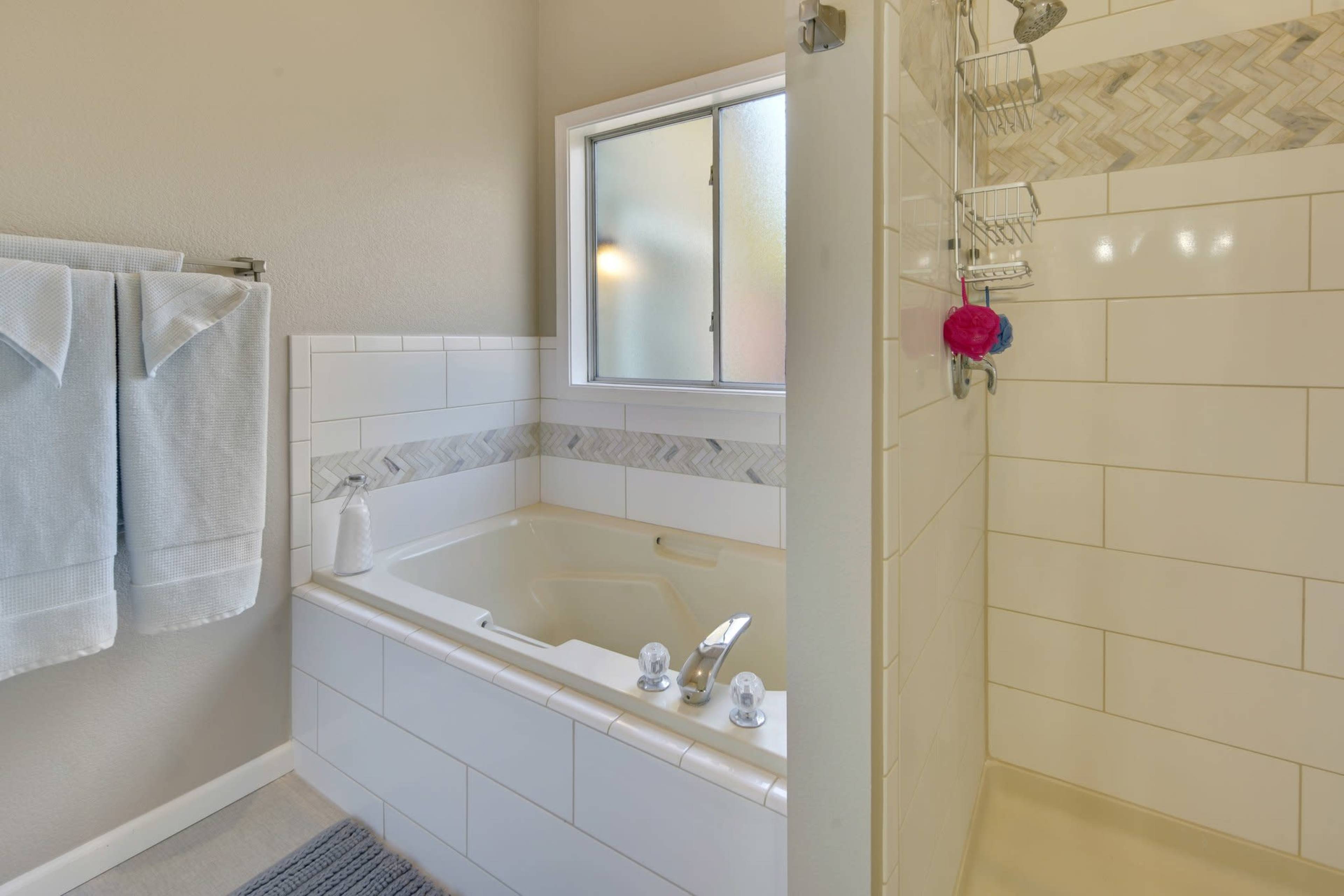 A bathroom featuring a jetted tub beside a glass-enclosed shower, with light-colored walls and a tiled backsplash.