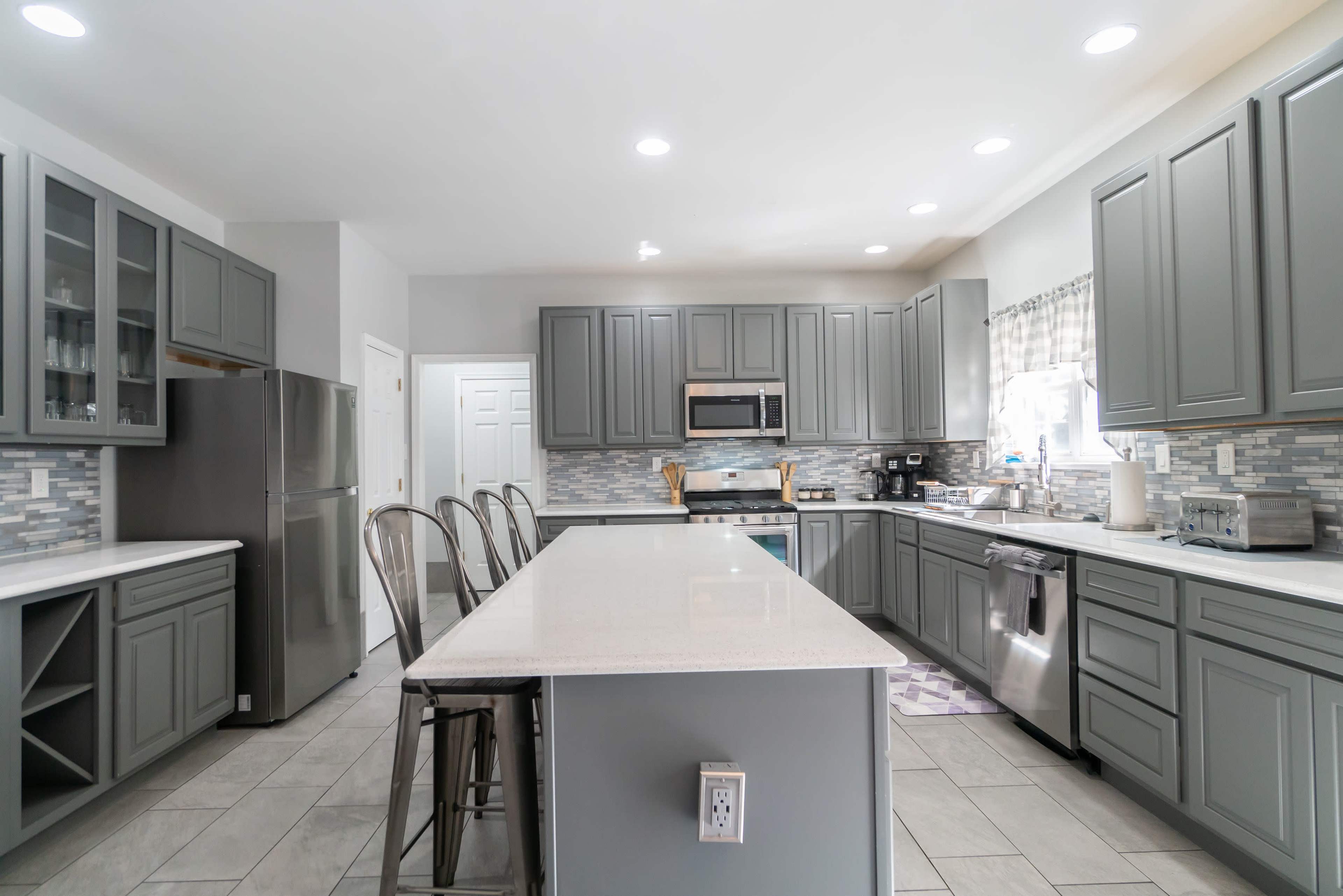 A modern kitchen features gray cabinets, stainless steel appliances, and a large island with bar stools.