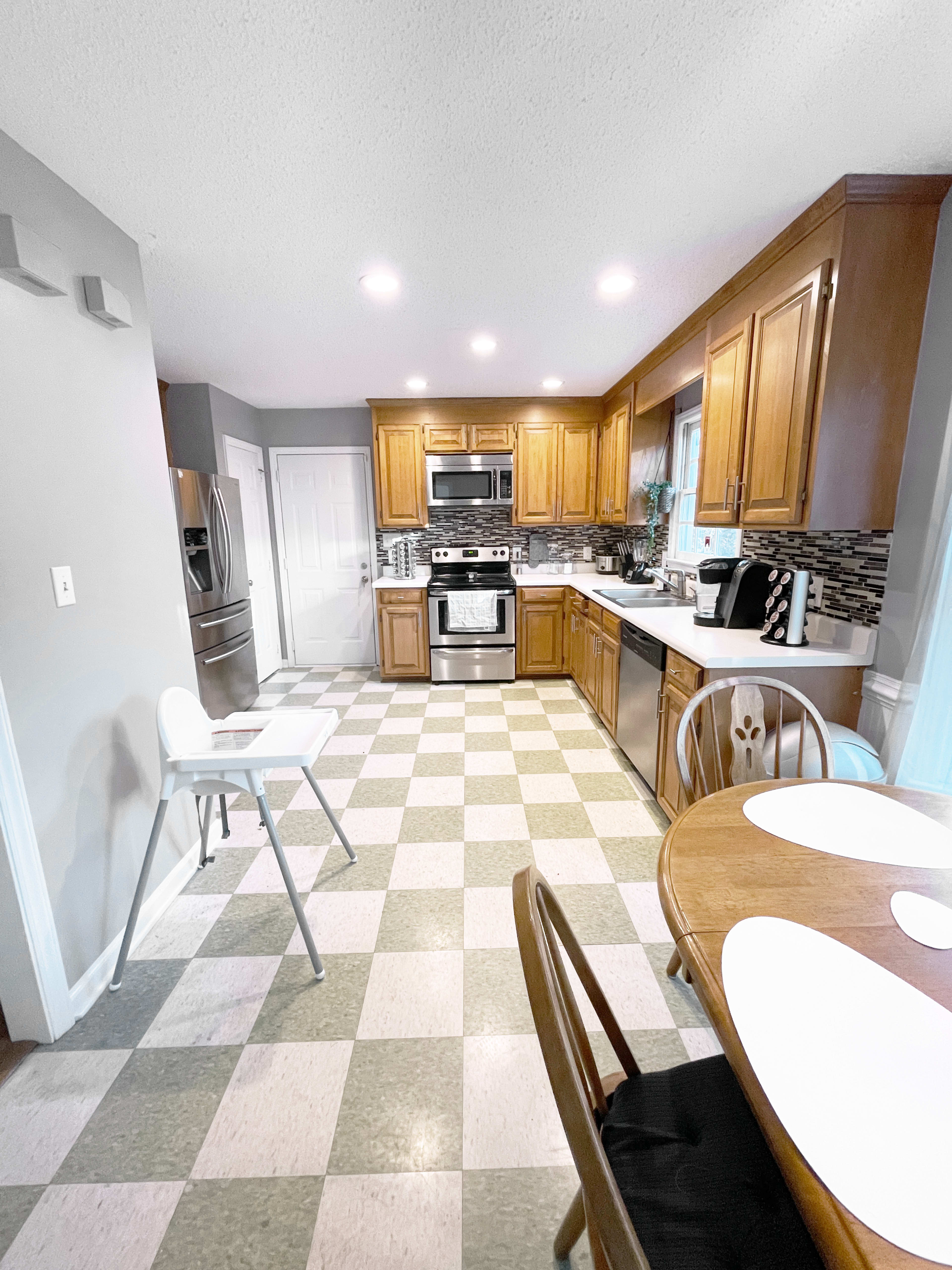 The image shows a modern kitchen with wooden cabinets, stainless steel appliances, and a checkered floor.