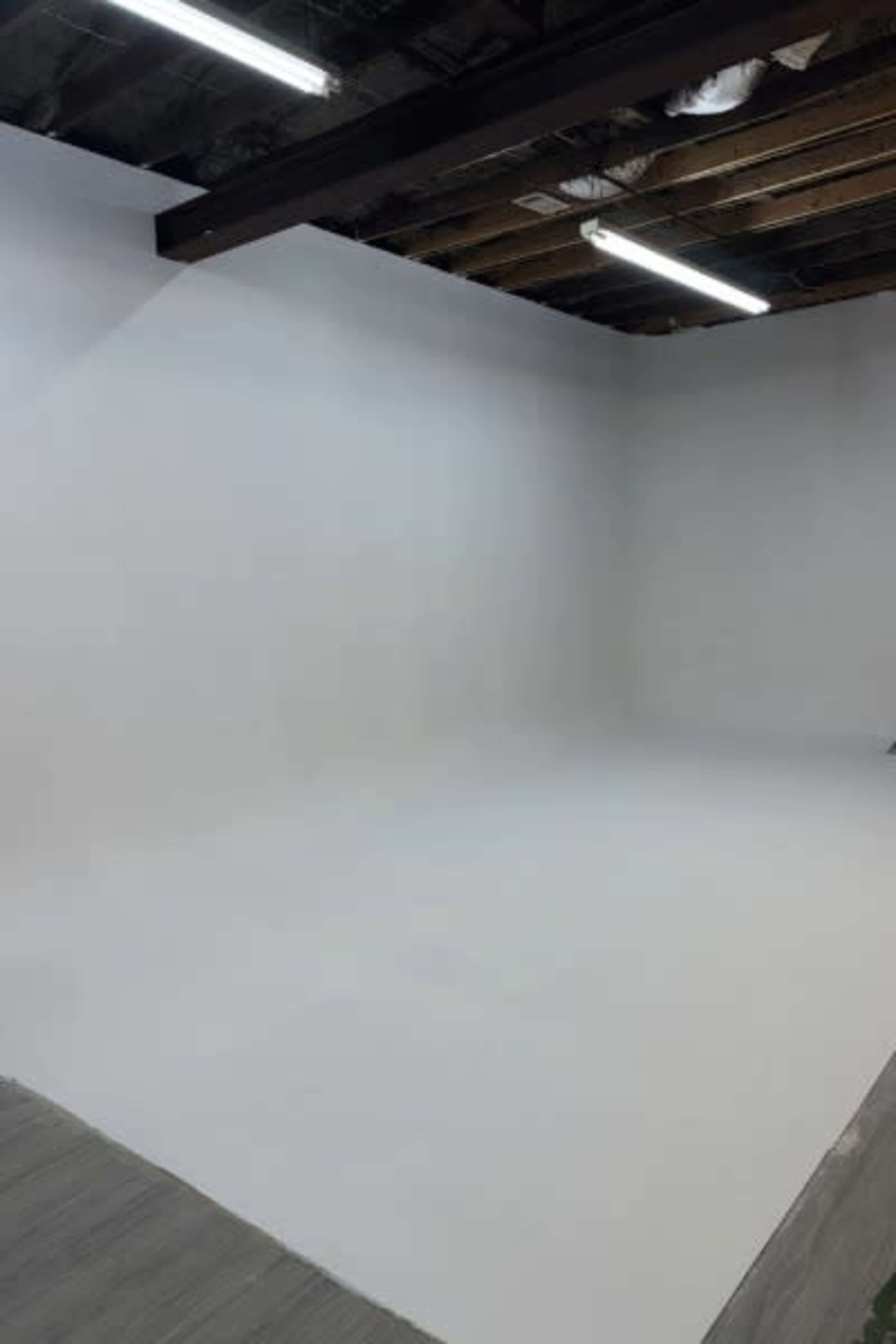 The image shows an empty room with white walls, a smooth floor, and exposed wooden beams overhead.