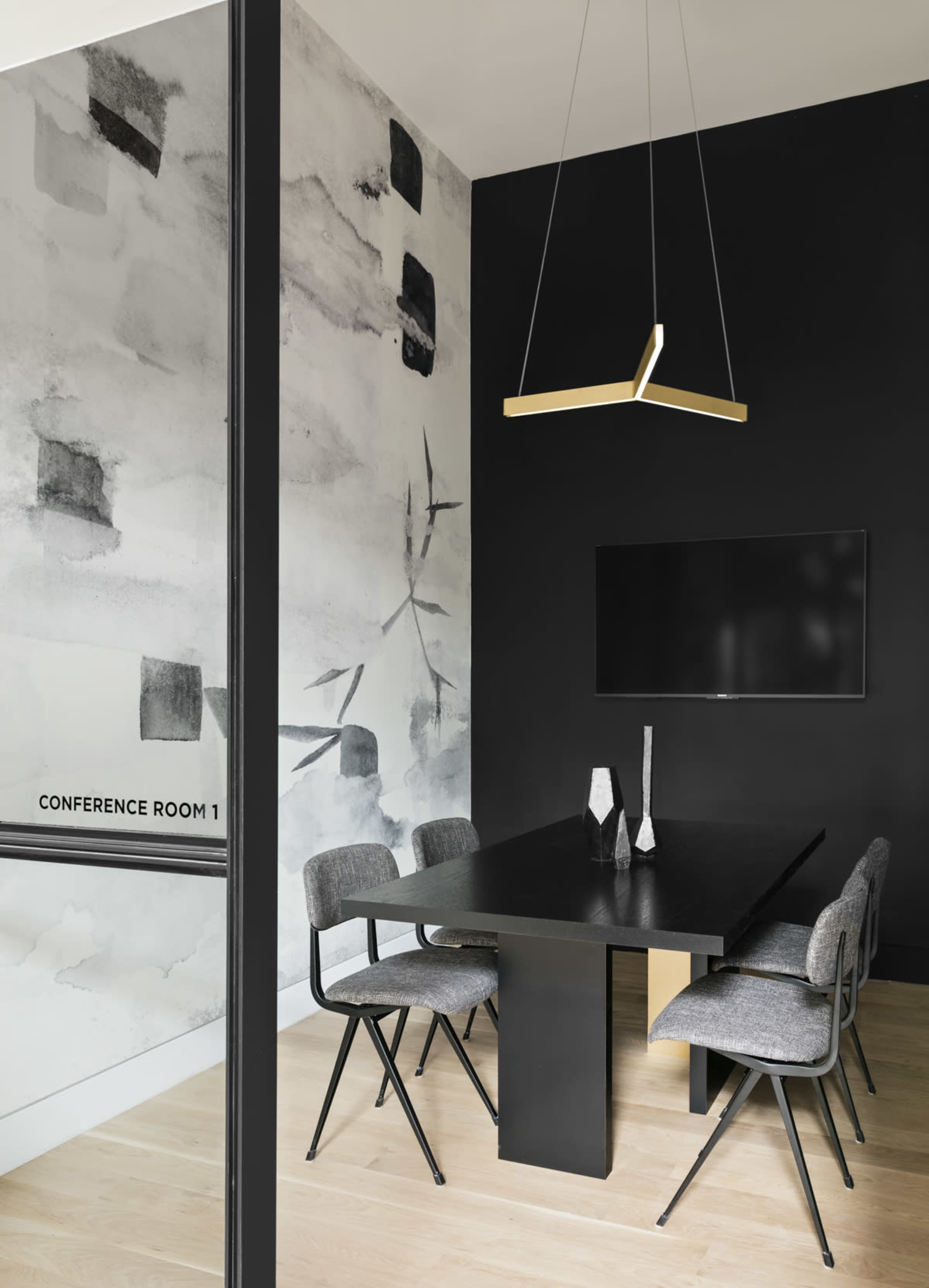 A modern conference room features a black wall with a mural, a rectangular table, and six chairs, illuminated by a geometric pendant light.