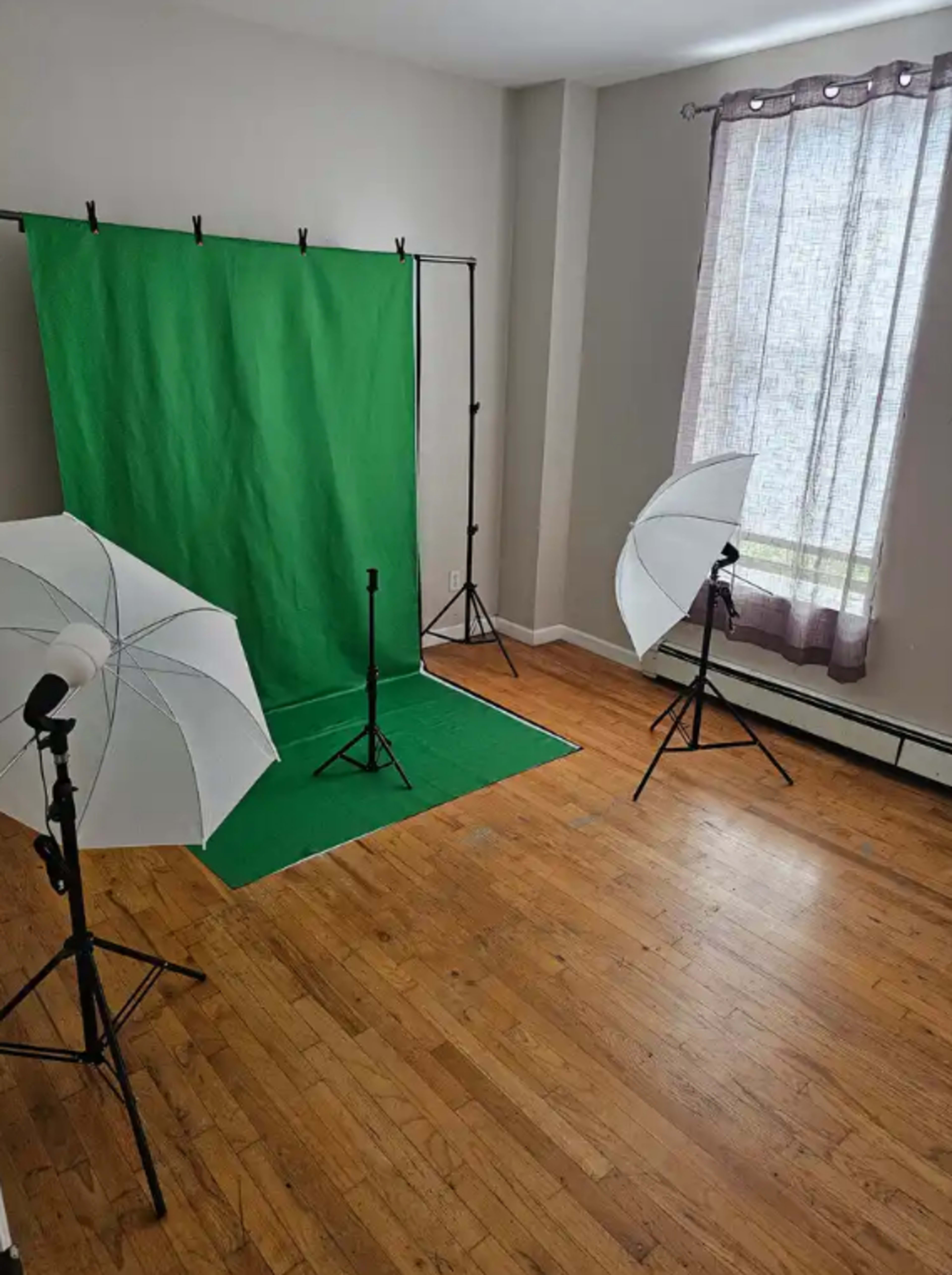 The image shows a well-lit room with a green backdrop set up for photography, along with two lighting umbrellas positioned on stands.