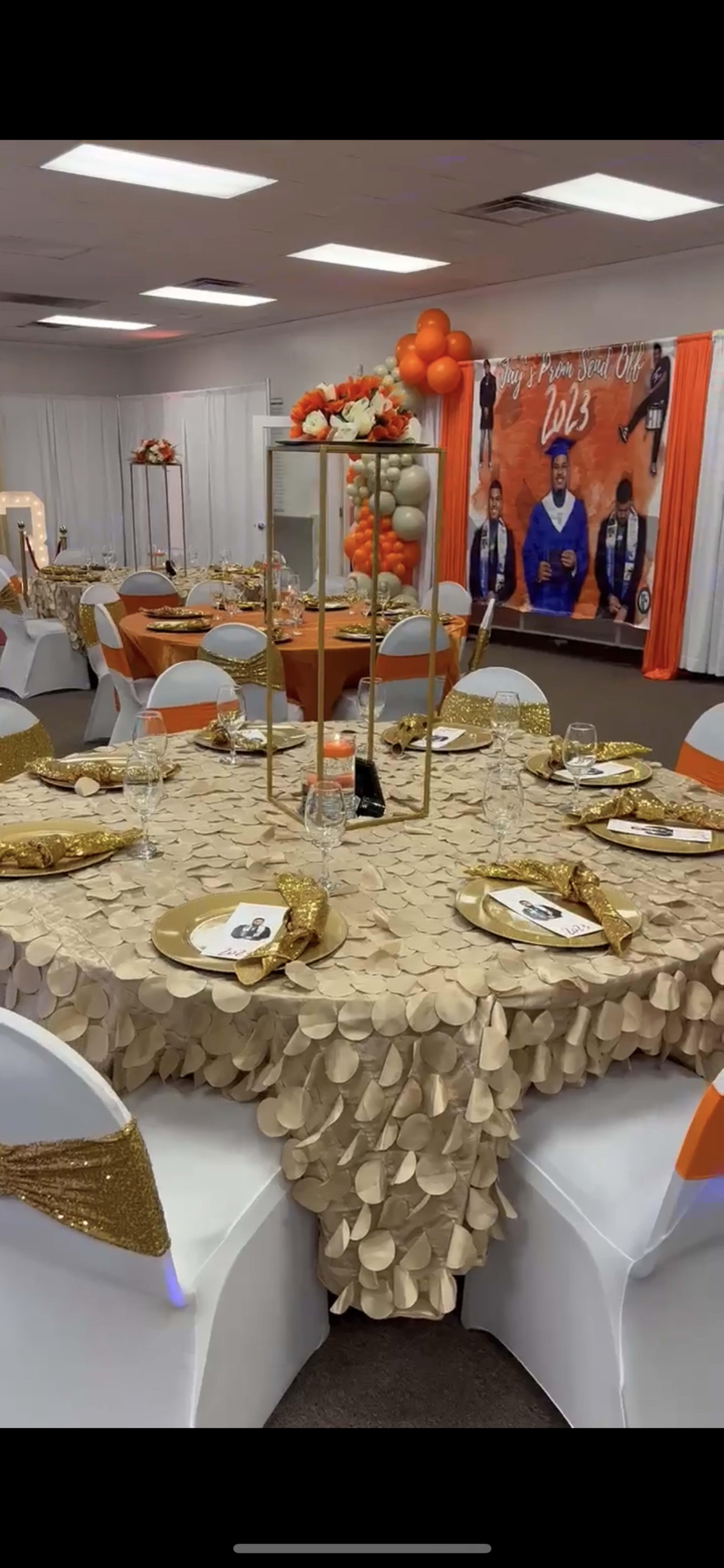 A banquet hall set up for an event, featuring round tables with gold tablecloths and decorations, with a backdrop displaying a group photo and the year "2023."