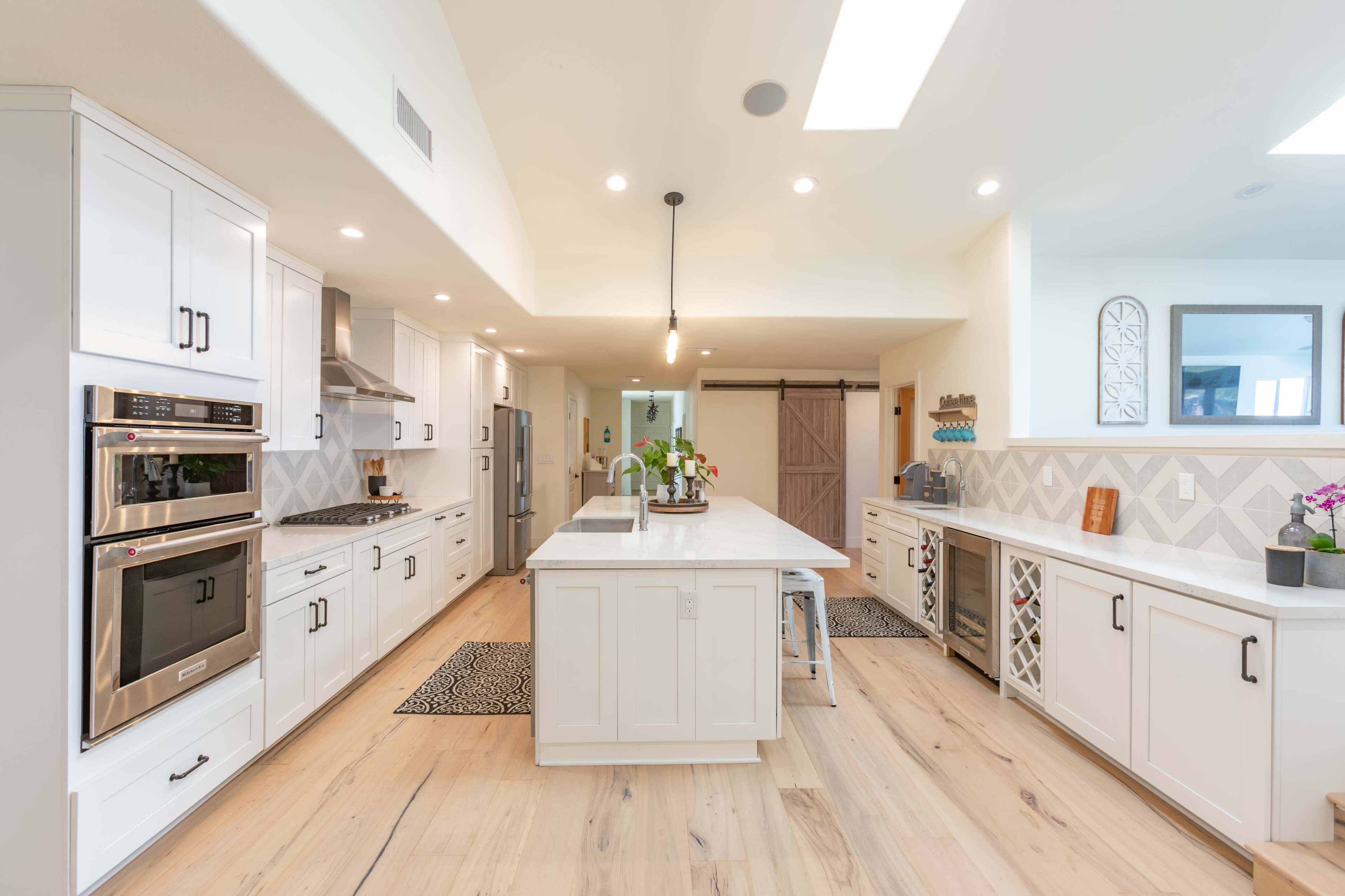 A modern kitchen features white cabinets, stainless steel appliances, and a large central island with pendant lighting.