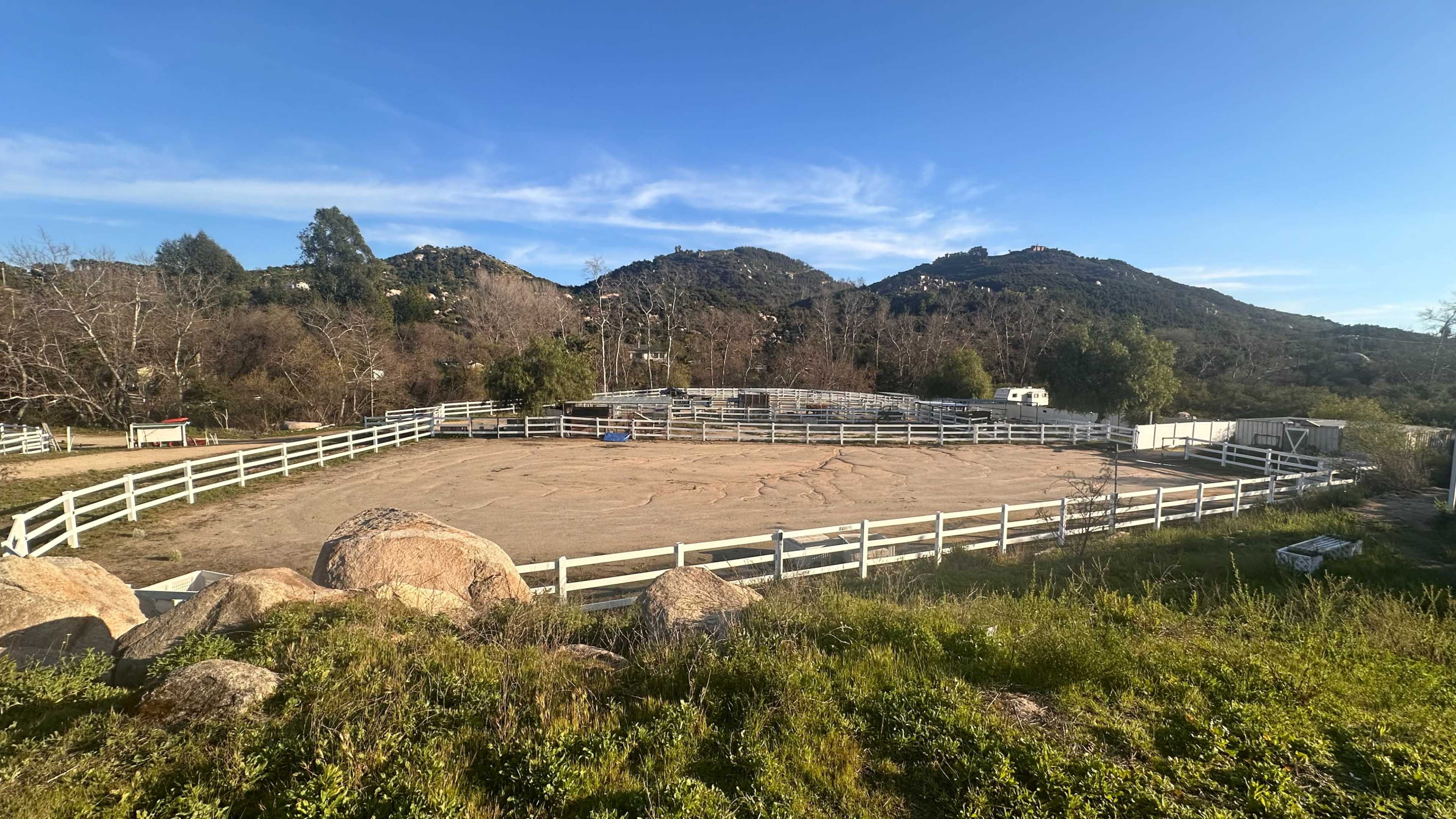 A fenced riding arena surrounded by hills and sparse vegetation.