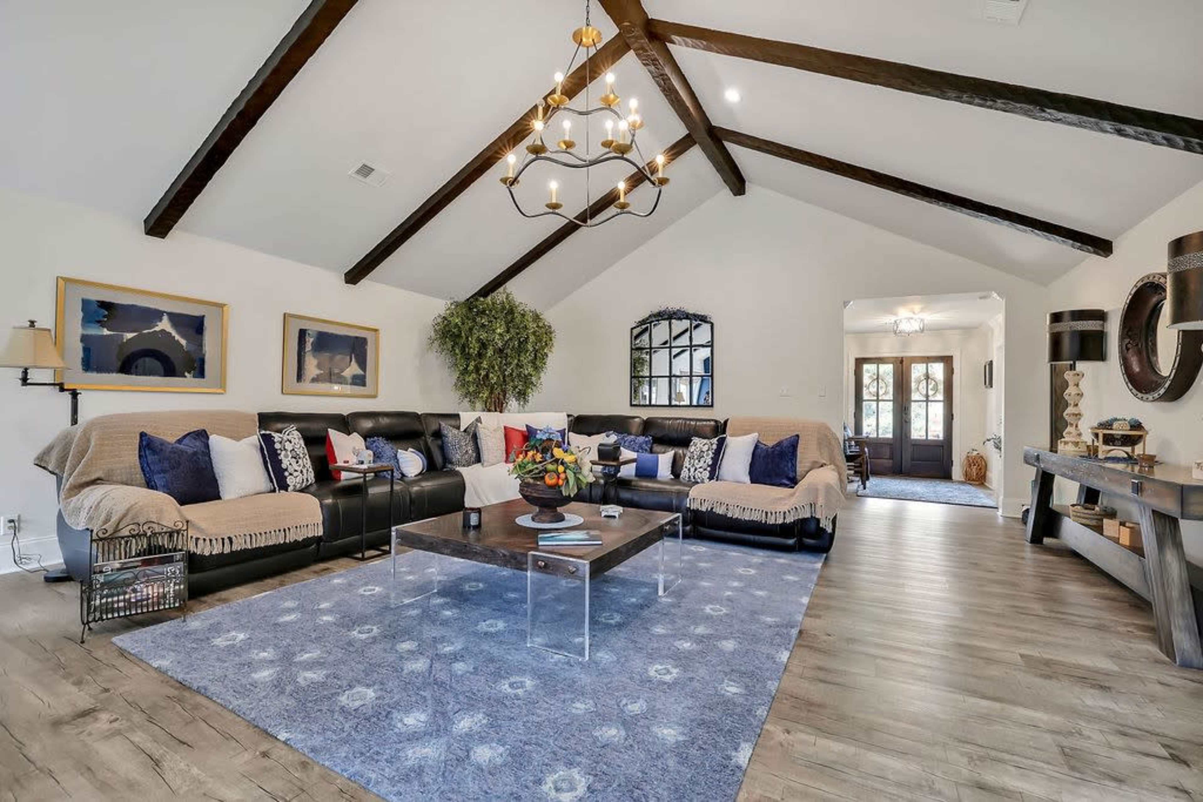 The living room features a black sectional sofa, a glass coffee table, and exposed wooden beams on the ceiling, with a decorative rug on the floor.