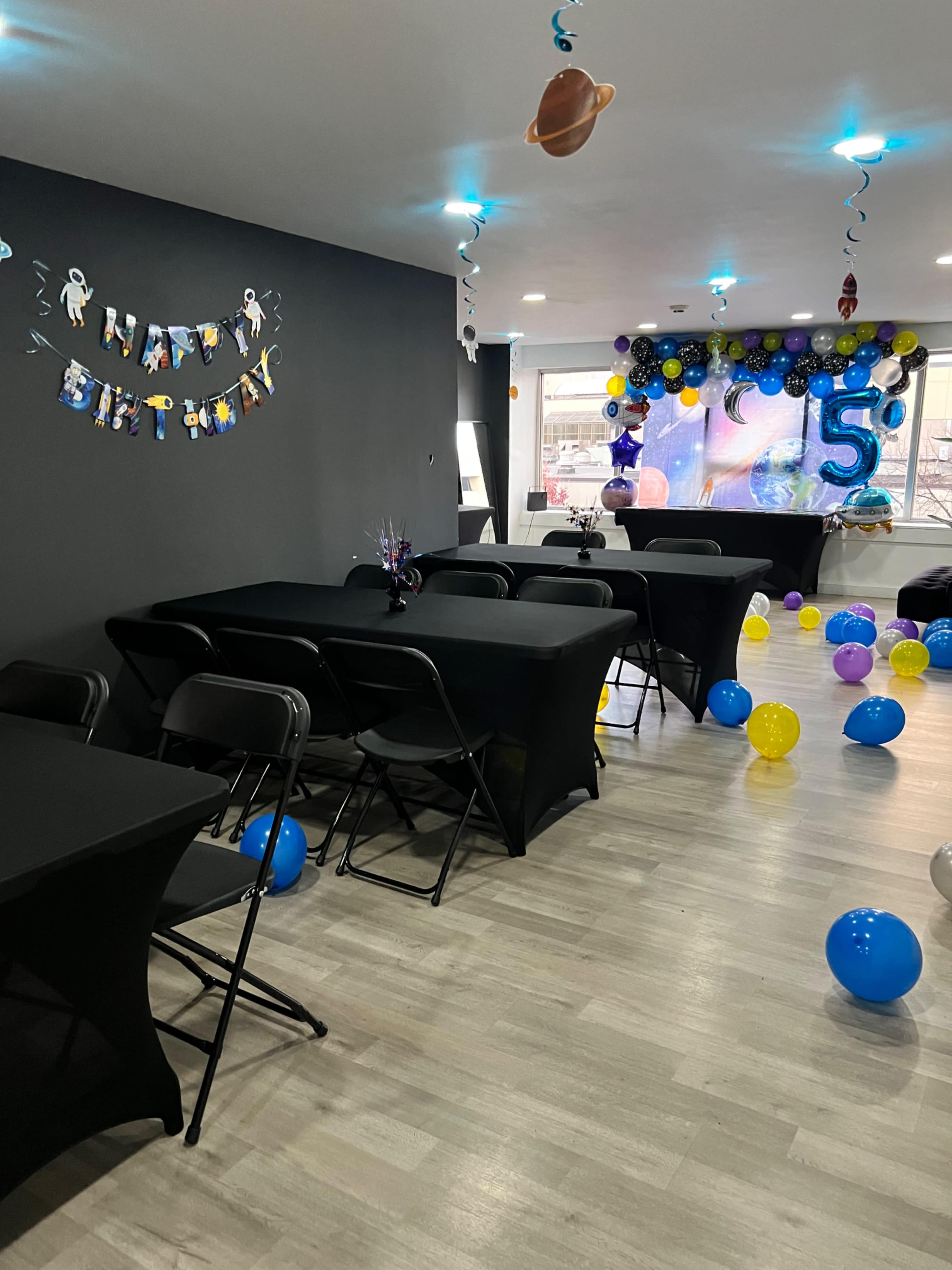 A decorated birthday party space with black tables, colorful balloons, and a backdrop displaying the number "5."
