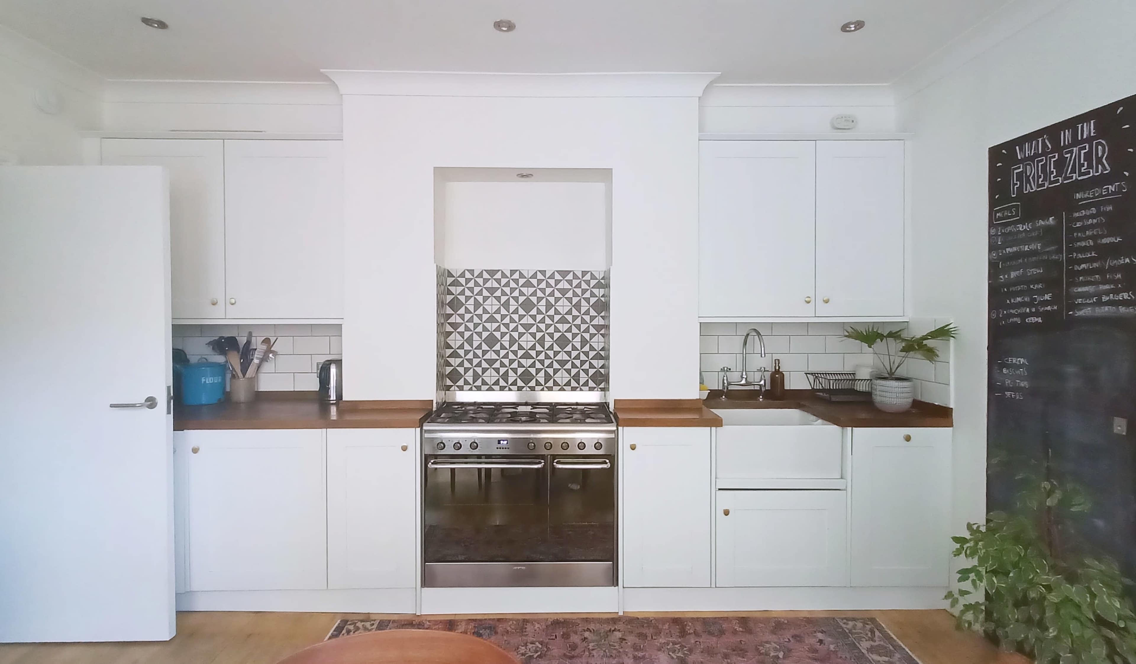 A modern kitchen with white cabinetry, a stainless steel stove, and a decorative backsplash featuring geometric tiles.