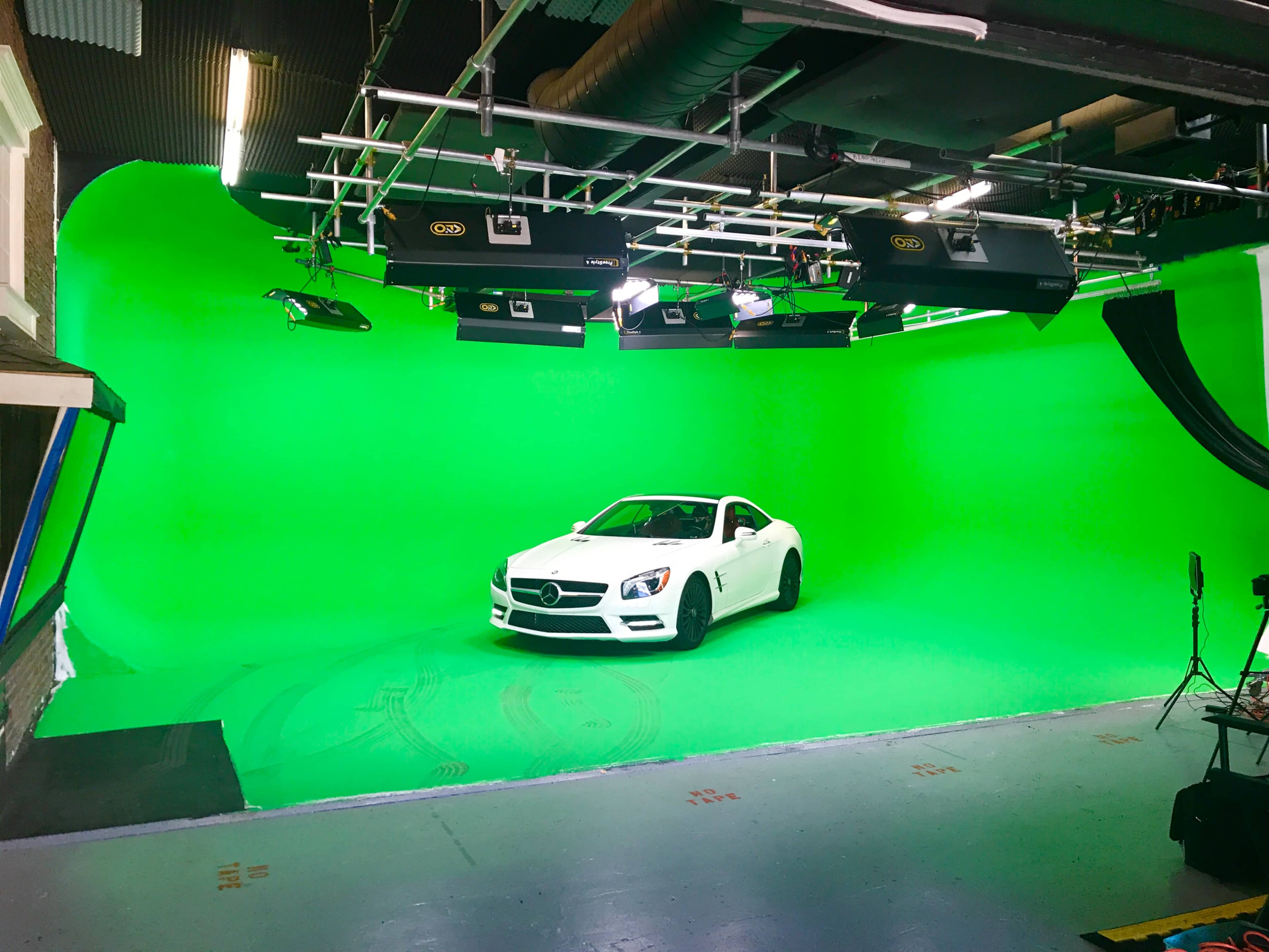 A white convertible car is parked in a studio with a green screen backdrop.