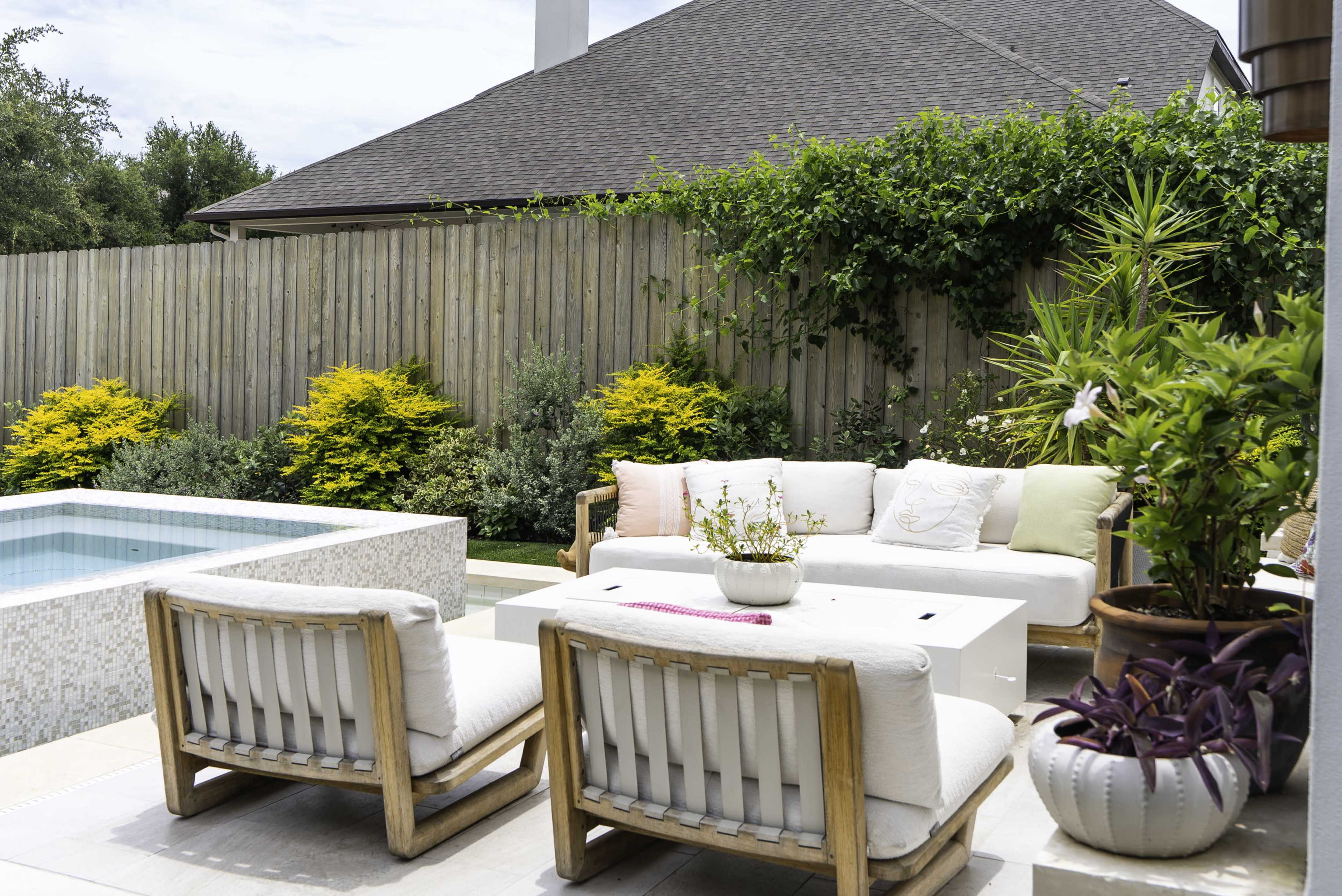 A modern outdoor lounge area features comfortable seating, a small table, and a swimming pool, surrounded by lush greenery.