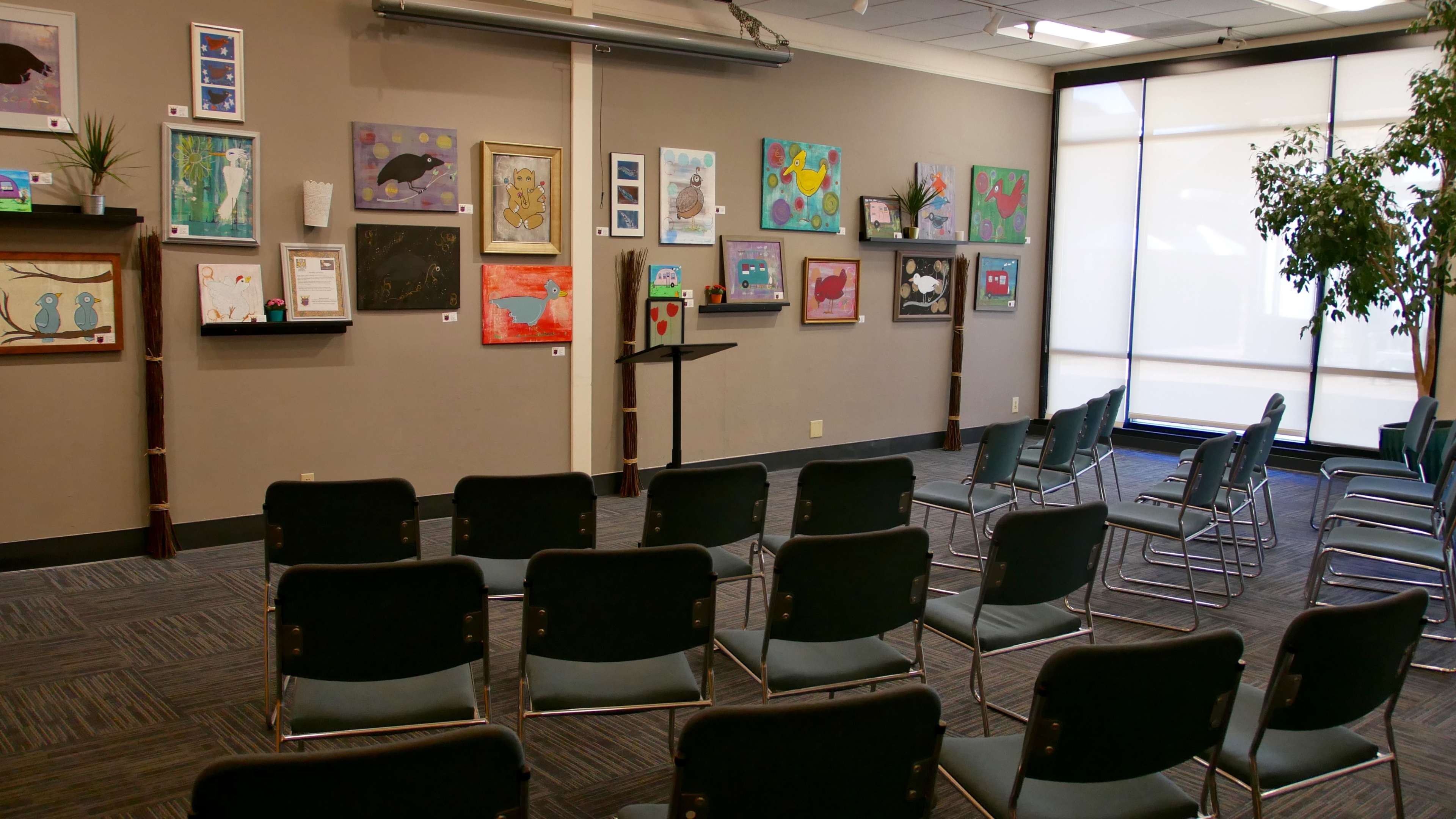 A room with several rows of chairs facing a podium, surrounded by framed artwork displayed on the walls.