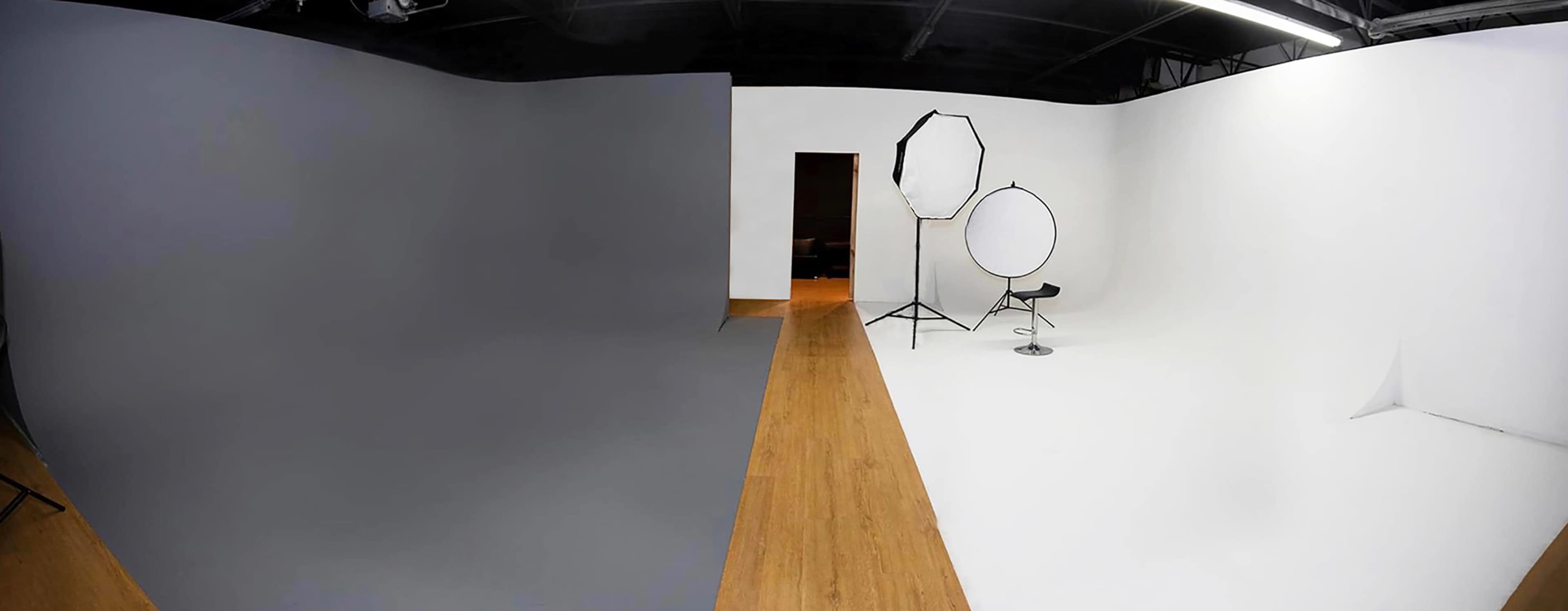 A photography studio with a gray backdrop on one side and a white backdrop on the other, featuring a chair and two lighting setups.