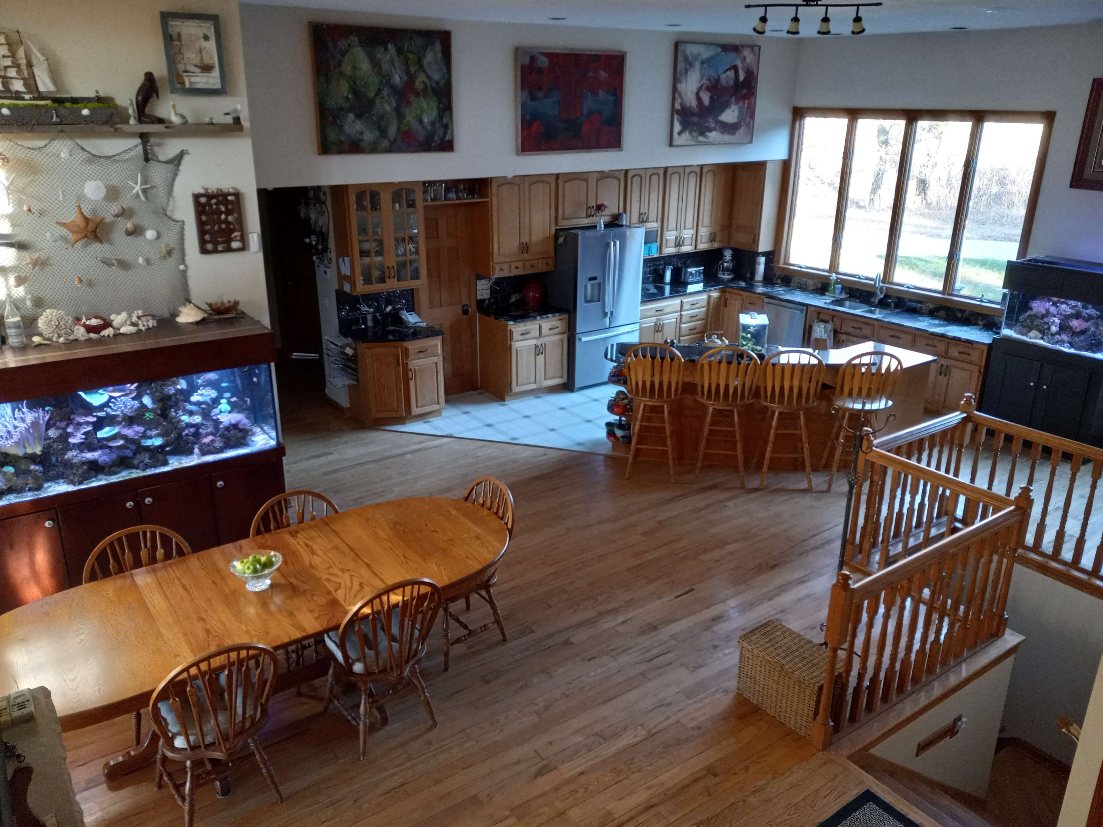 A spacious open-concept kitchen and dining area features wooden cabinetry, a large dining table, and two fish tanks beside a set of windows.
